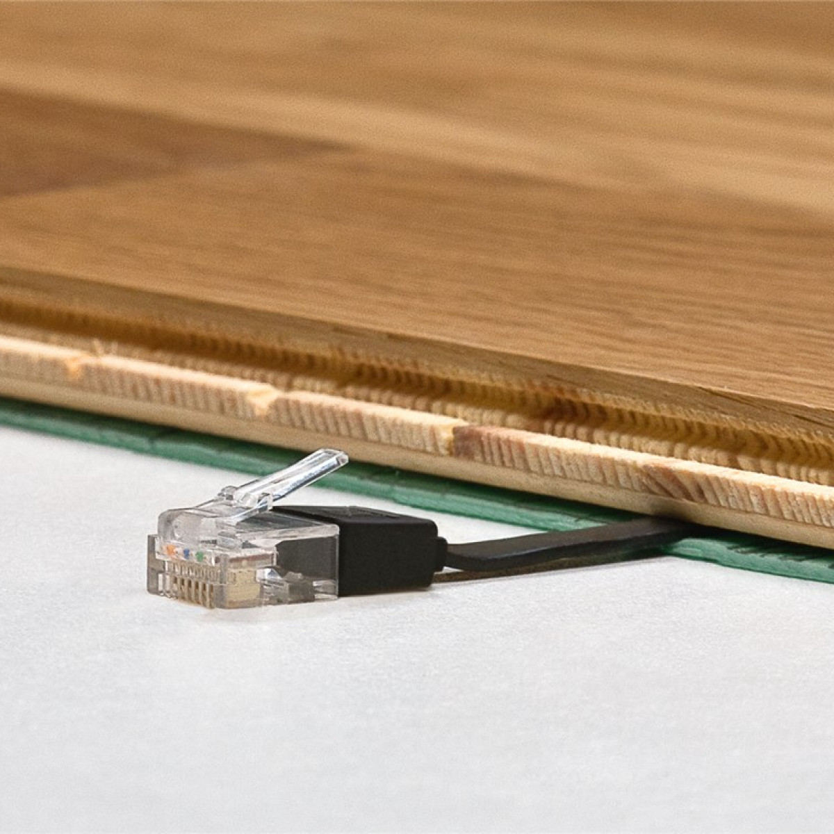 Close-up van een netwerkkabel aangesloten op een houten vloer, met een wit oppervlak.
