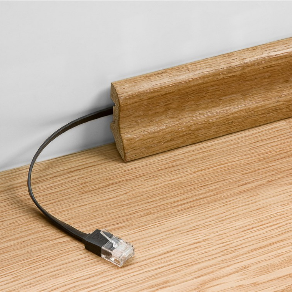Een zwarte netwerkkabel is aangesloten op een houten plint op een houten vloer. Witte muur achtergrond.
