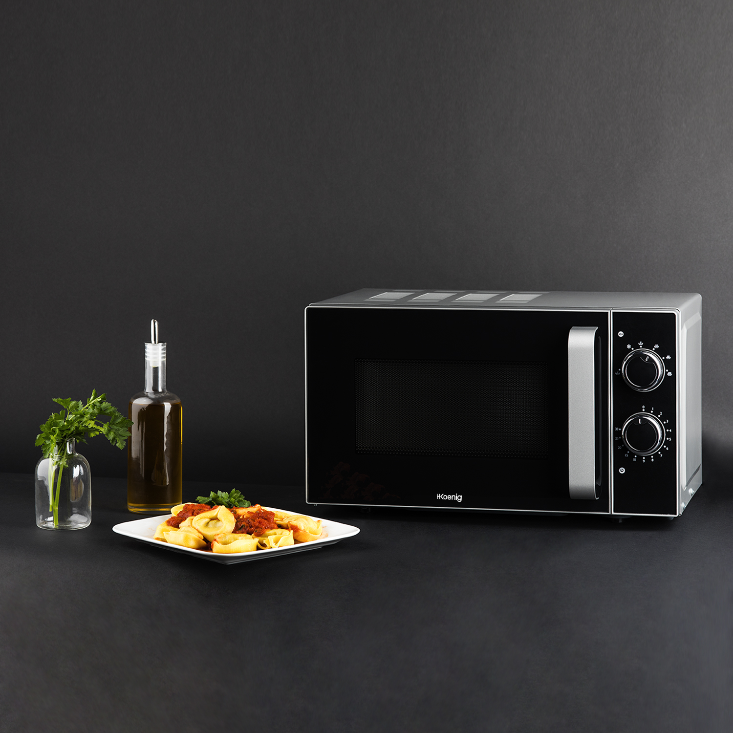 Czarna kuchenka mikrofalowa z jedzeniem na talerzu. Oliwa z oliwek i pietruszka obok na czarnej powierzchni.