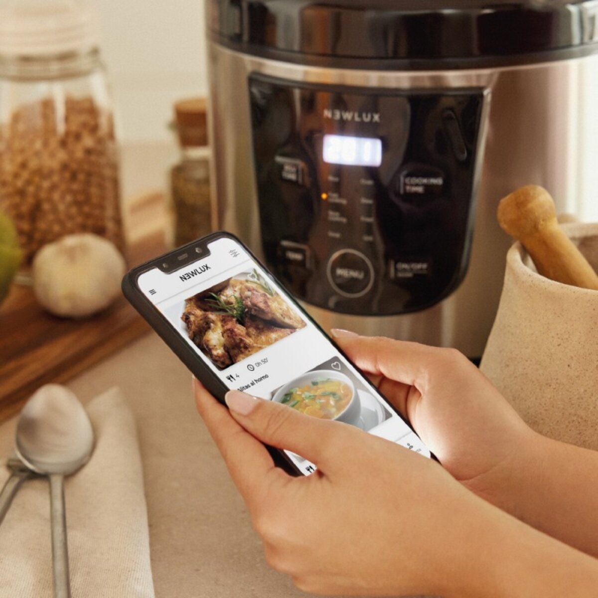 Mani che tengono un telefono con un'app di ricette aperta. Una pentola e dei cucchiai sono vicini.