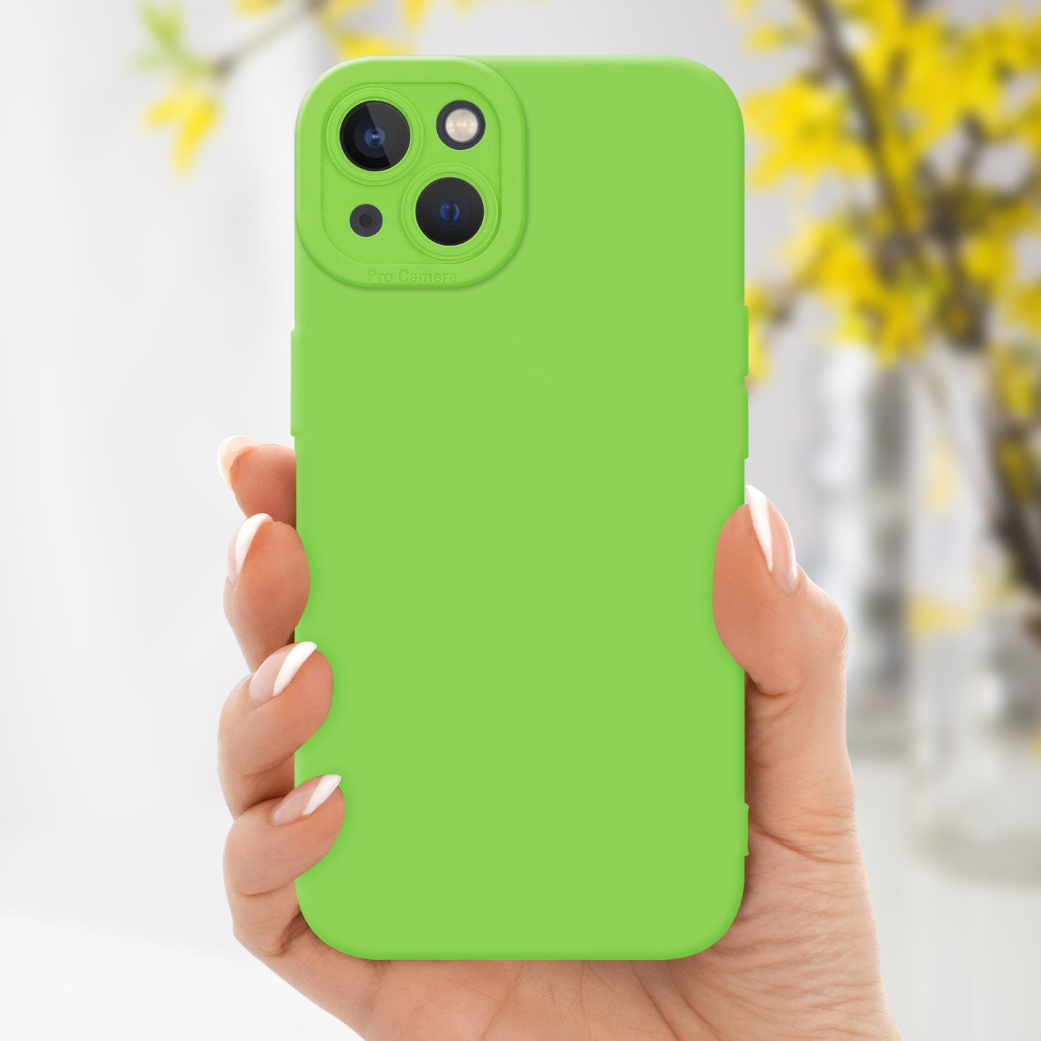 Mano che tiene una custodia verde brillante con tripla fotocamera, fiori gialli sullo sfondo.