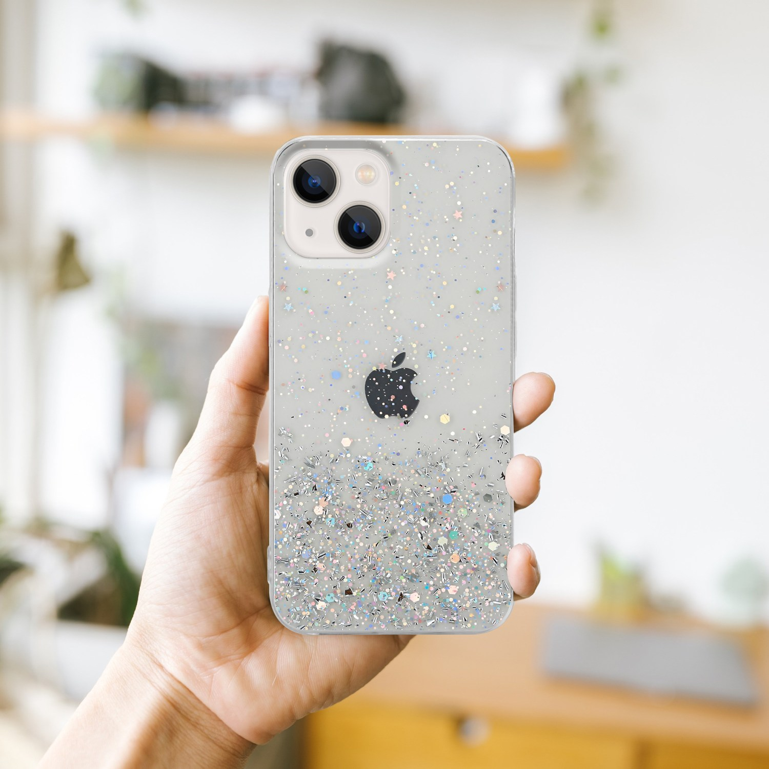 Eine Hand, die eine transparente Glitzer-Handyhülle mit einem Apple-Logo hält. Verschwommener Hintergrund.