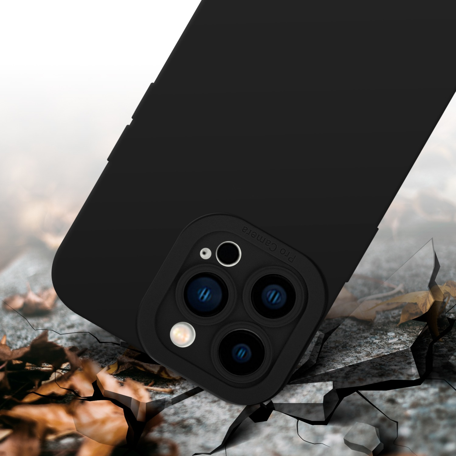 Custodia nera per telefono con tripla fotocamera che cade su superficie crepata, con foglie sparse.