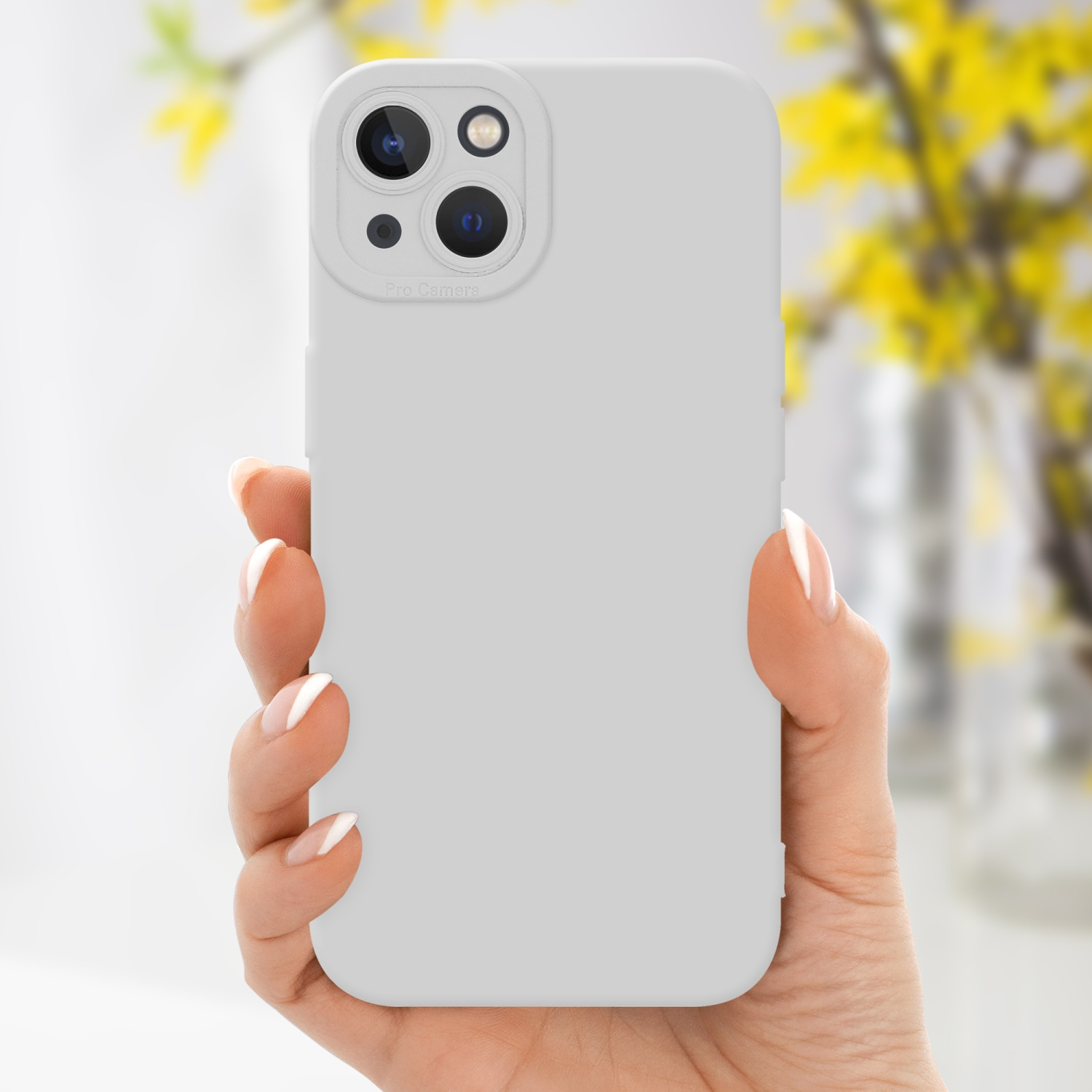 La mano di una donna che tiene una custodia bianca con un rigonfiamento della fotocamera e un vaso di fiori giallo sullo sfondo.