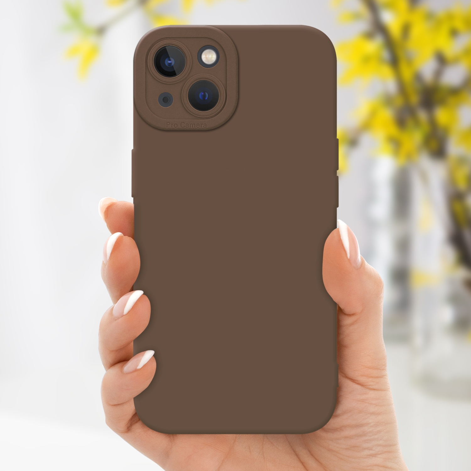 Una mano che tiene una custodia marrone per telefono con ritaglio per tripla fotocamera, fiori gialli sullo sfondo.