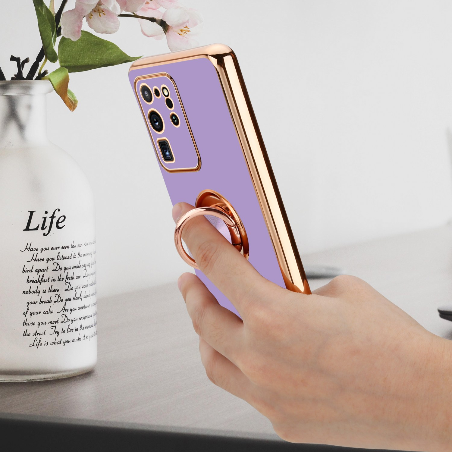 Una mano che tiene una custodia per telefono viola con cornice dorata e anello di supporto.