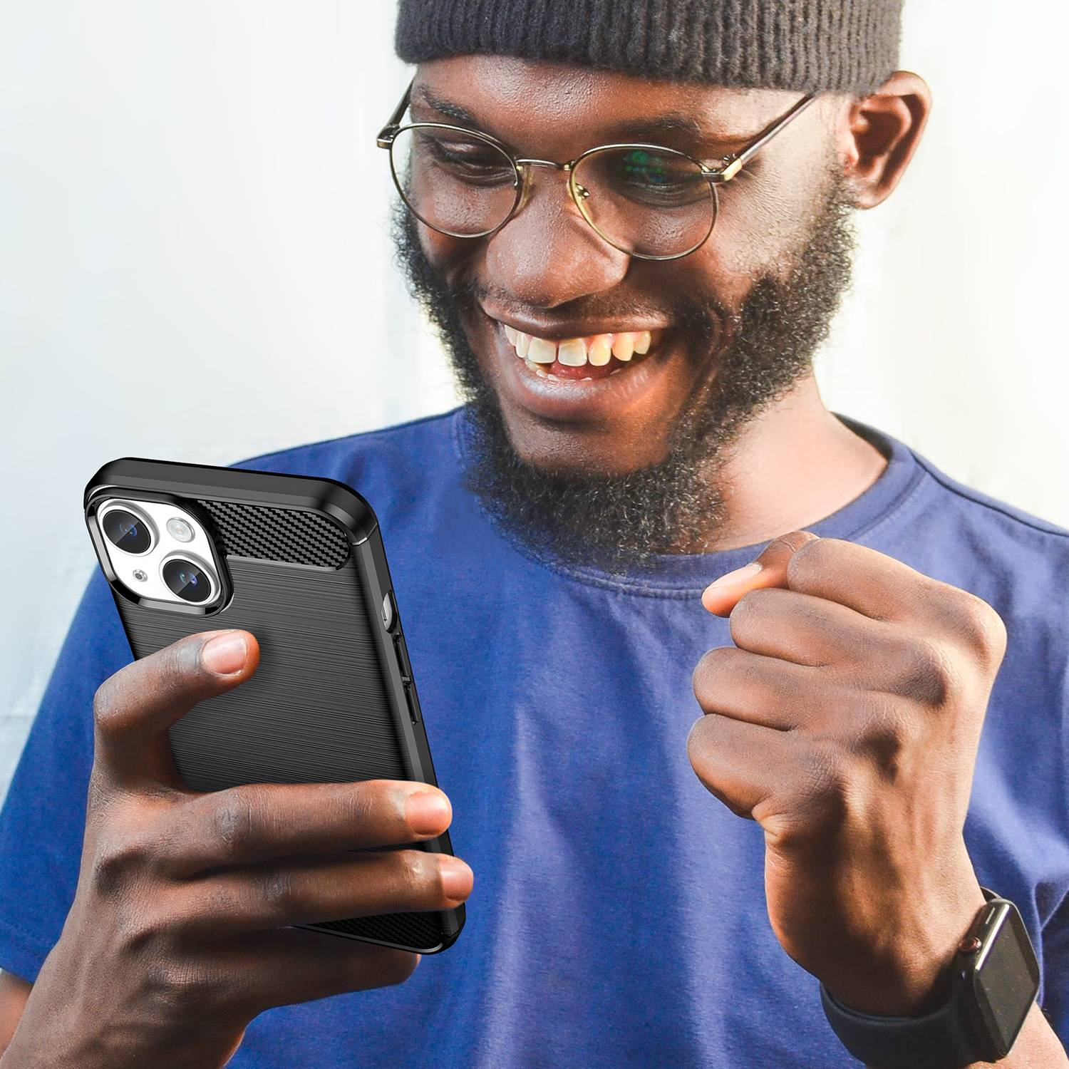 Ein lächelnder Mann hält ein schwarzes Telefon mit einer strukturierten Hülle. Er trägt eine Brille und ein blaues Hemd.
