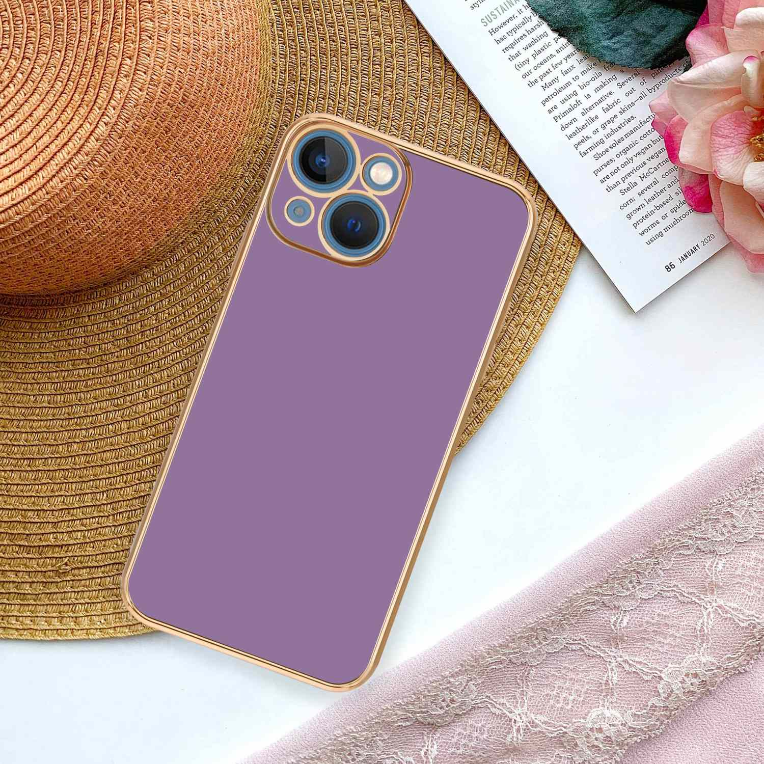 Eine lila Handyhülle auf einer Strohmatte, mit einer Zeitschrift und rosa Spitze. Das Telefon zeigt eine Kamera.