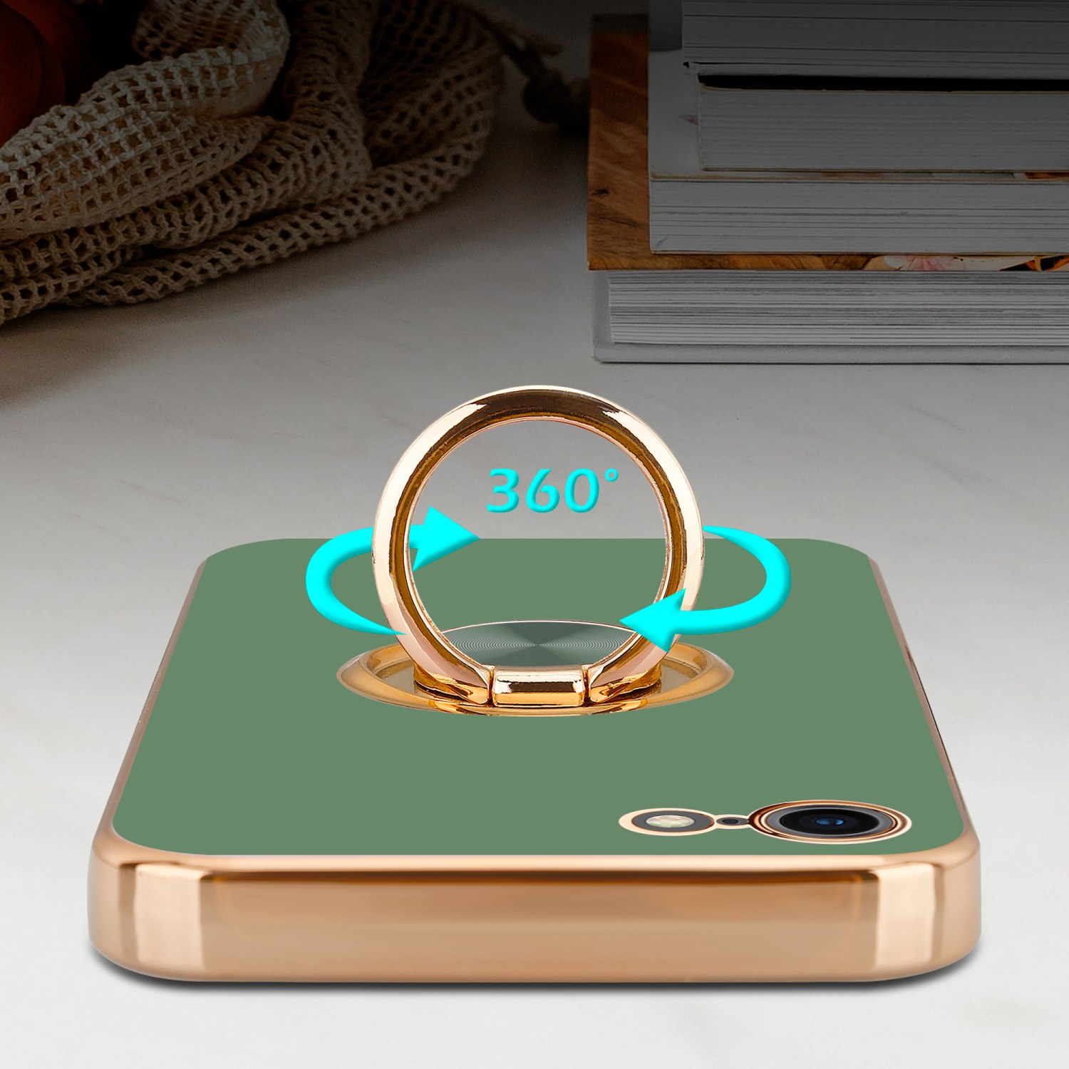 Grüne Handyhülle mit einem goldenen Ring, der sich um 360 Grad dreht. Weißer Tisch, Bücher und Hintergrund.