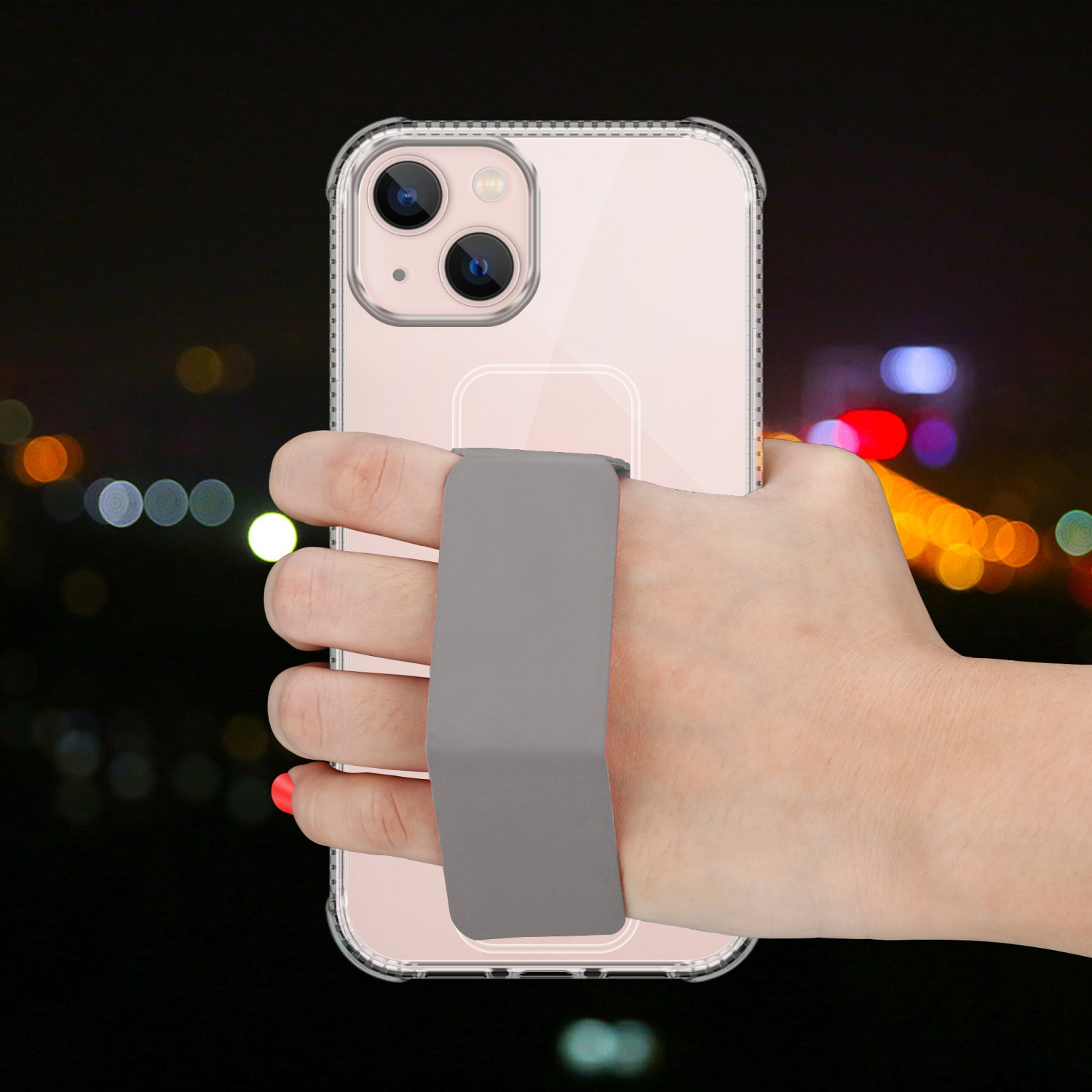 Hand hält ein Telefon mit grauem Riemen. Der Hintergrund ist eine verschwommene Nachtszene.