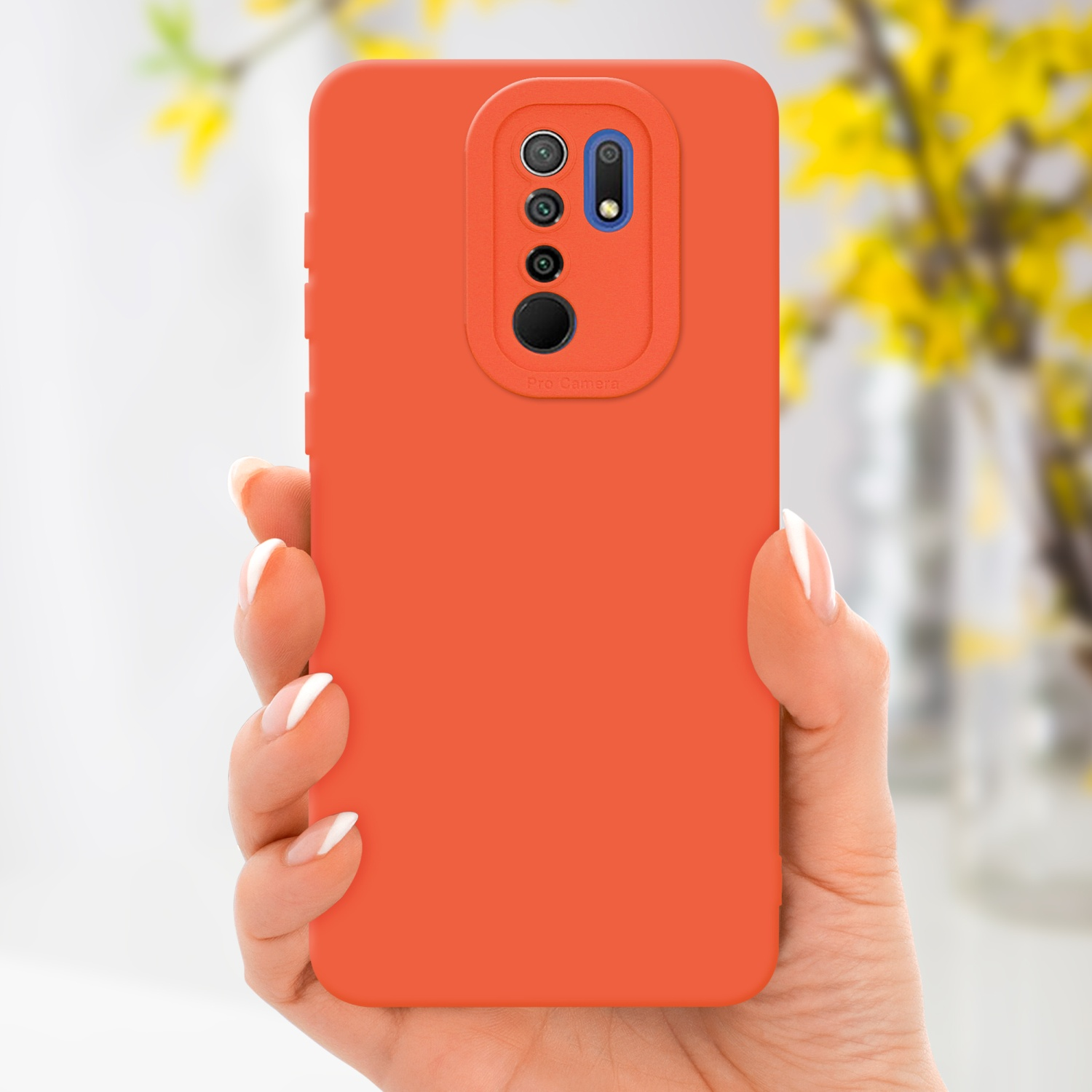 Main tenant une coque de téléphone orange. Fleurs jaunes en arrière-plan. Coque avec bosse de caméra.
