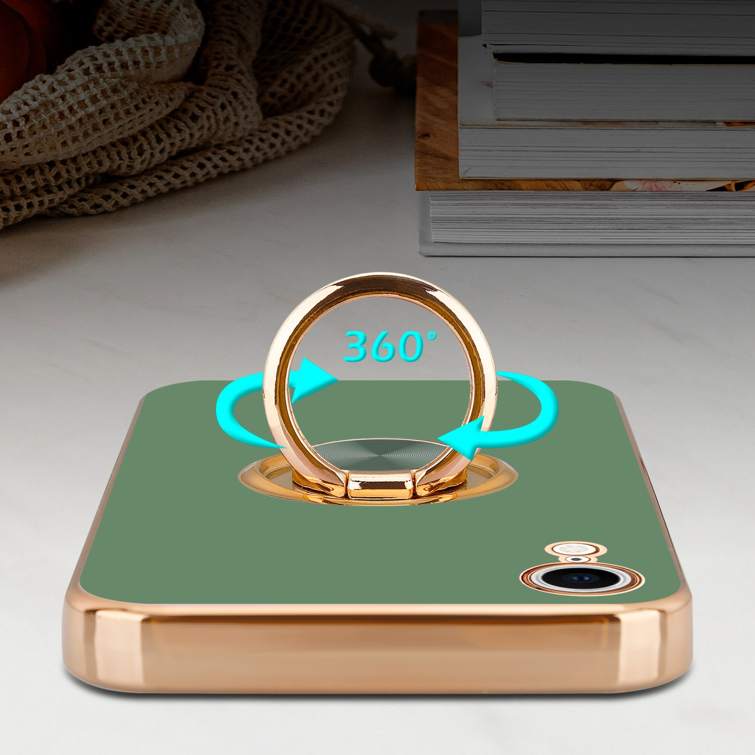 Grüne Handyhülle mit goldenem Ringhalter, 360°-Drehpfeil und verschwommenem Buchhintergrund.