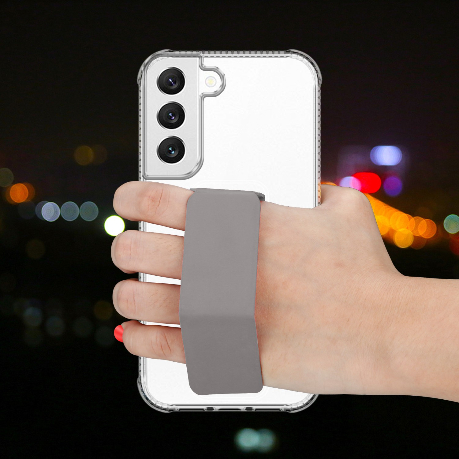 Hand hält ein Telefon mit grauem Riemen. Der Hintergrund zeigt verschwommene Stadtlichter bei Nacht.