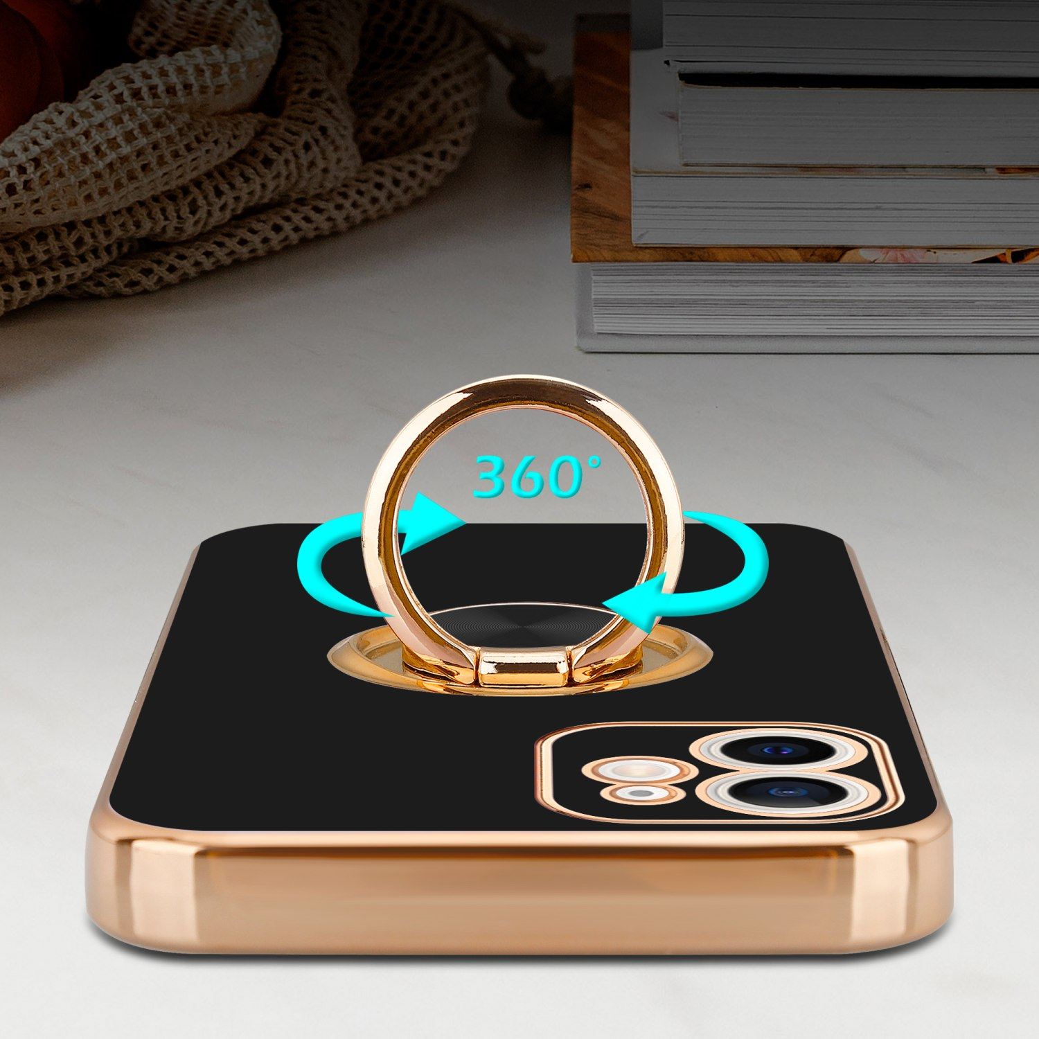 Schwarzes Telefon mit goldenem Ringhalter, zeigt 360-Grad-Drehung. Bücher auf einem Tisch im Hintergrund.