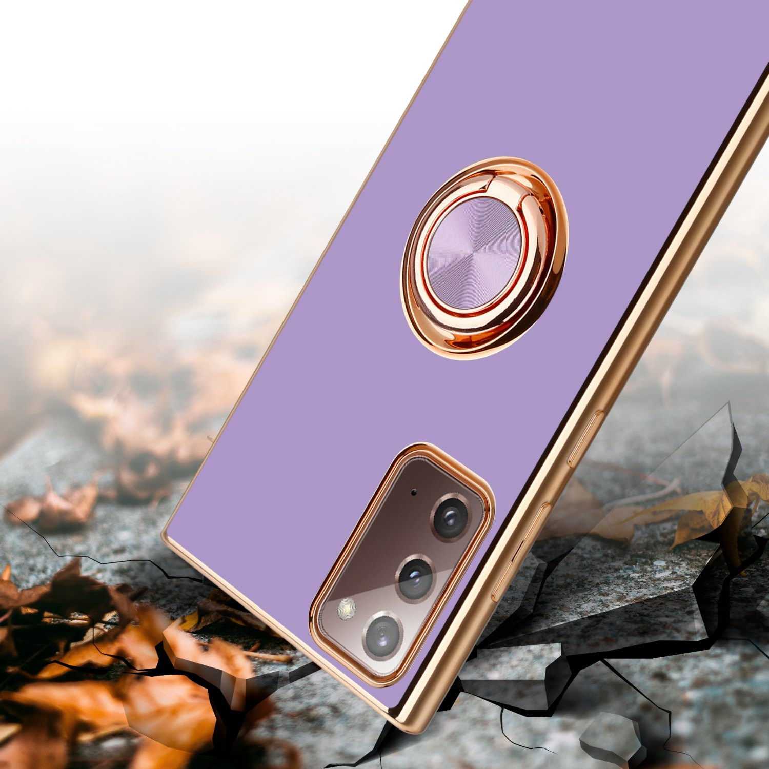 Custodia viola per telefono con anello dorato, su una superficie crepata. Foglie autunnali intorno.