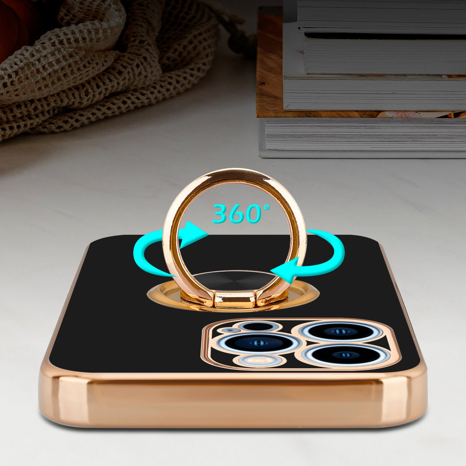 Schwarze Handyhülle mit goldenem Ringhalter, 360° Drehung, auf weißem Tisch, Bücherstapel im Hintergrund.