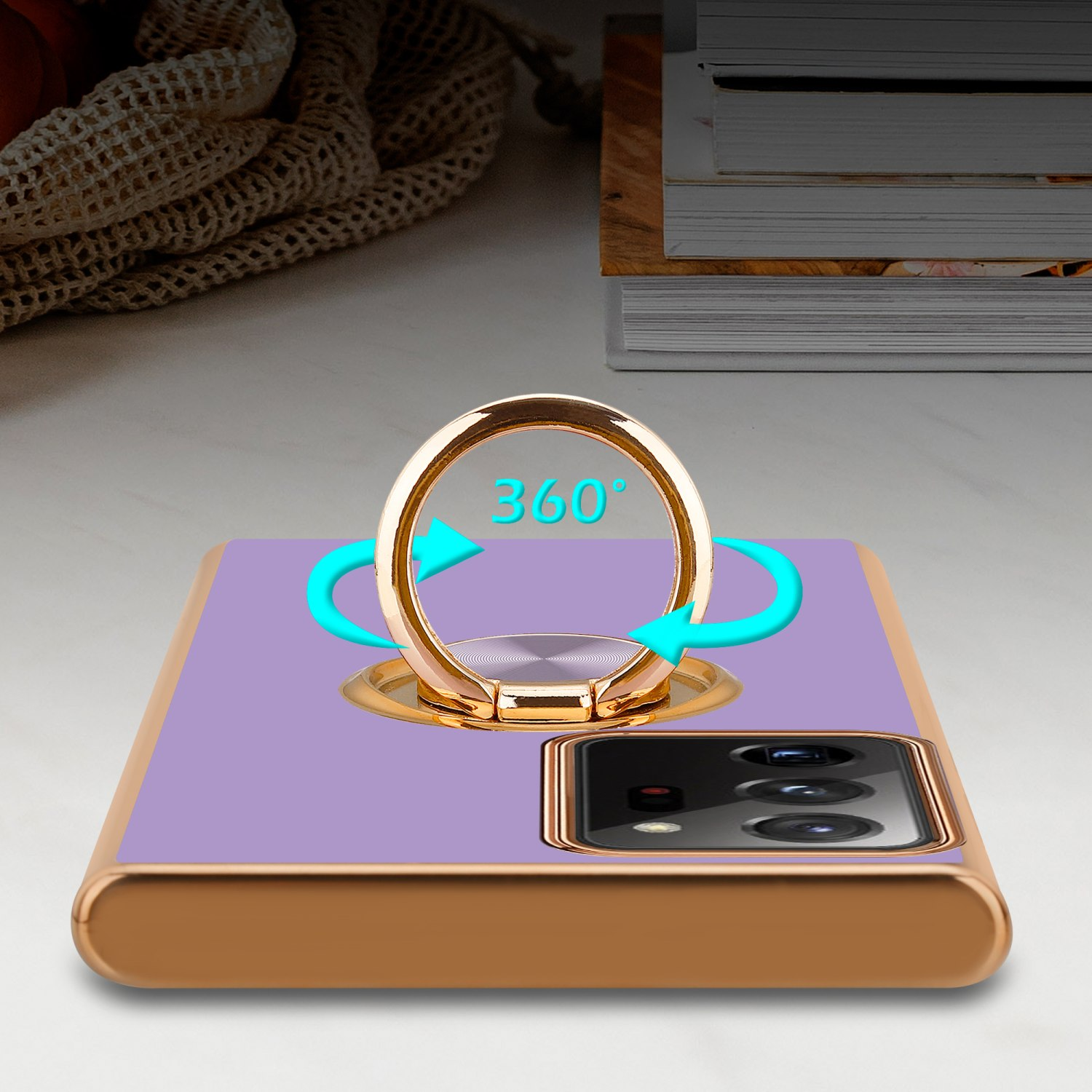 Lila Telefon mit goldenem Ringhalter, zeigt 360-Grad-Drehung. Bücher auf einem Tisch im Hintergrund.
