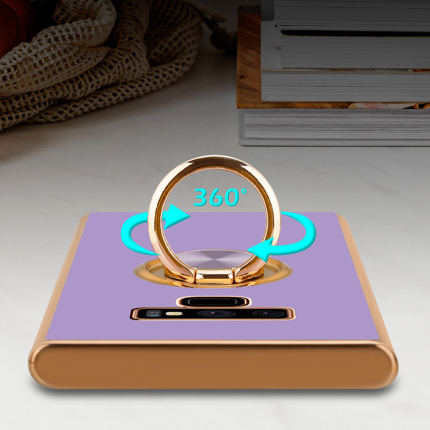 Una custodia per telefono con un porta anello dorato con frecce. Lo sfondo è di colore lilla chiaro.