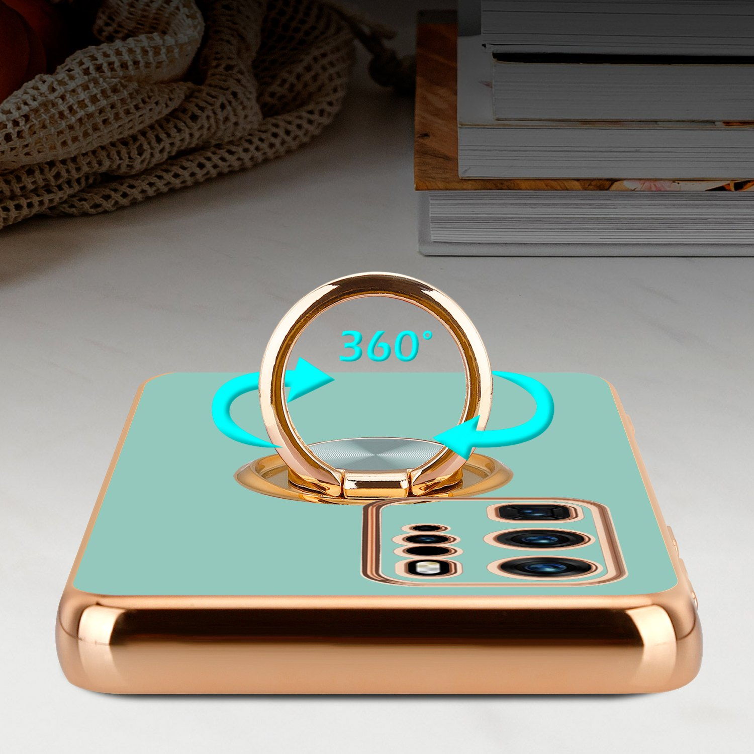Minzfarbene Handyhülle mit goldenem Ring und Telefon mit goldenem Rahmen, auf weißer Oberfläche.