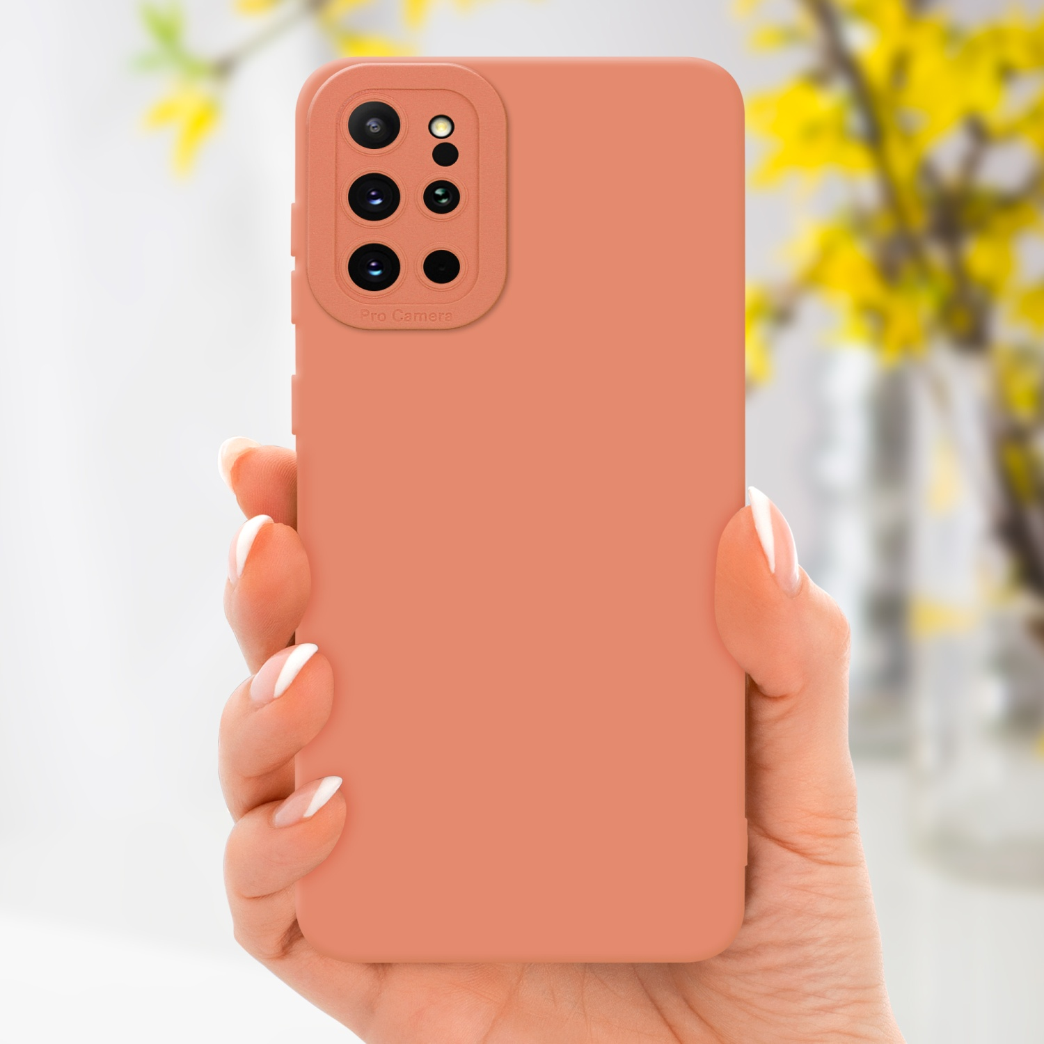Una mano che tiene una custodia per telefono color corallo, con un vaso di fiori giallo sullo sfondo.