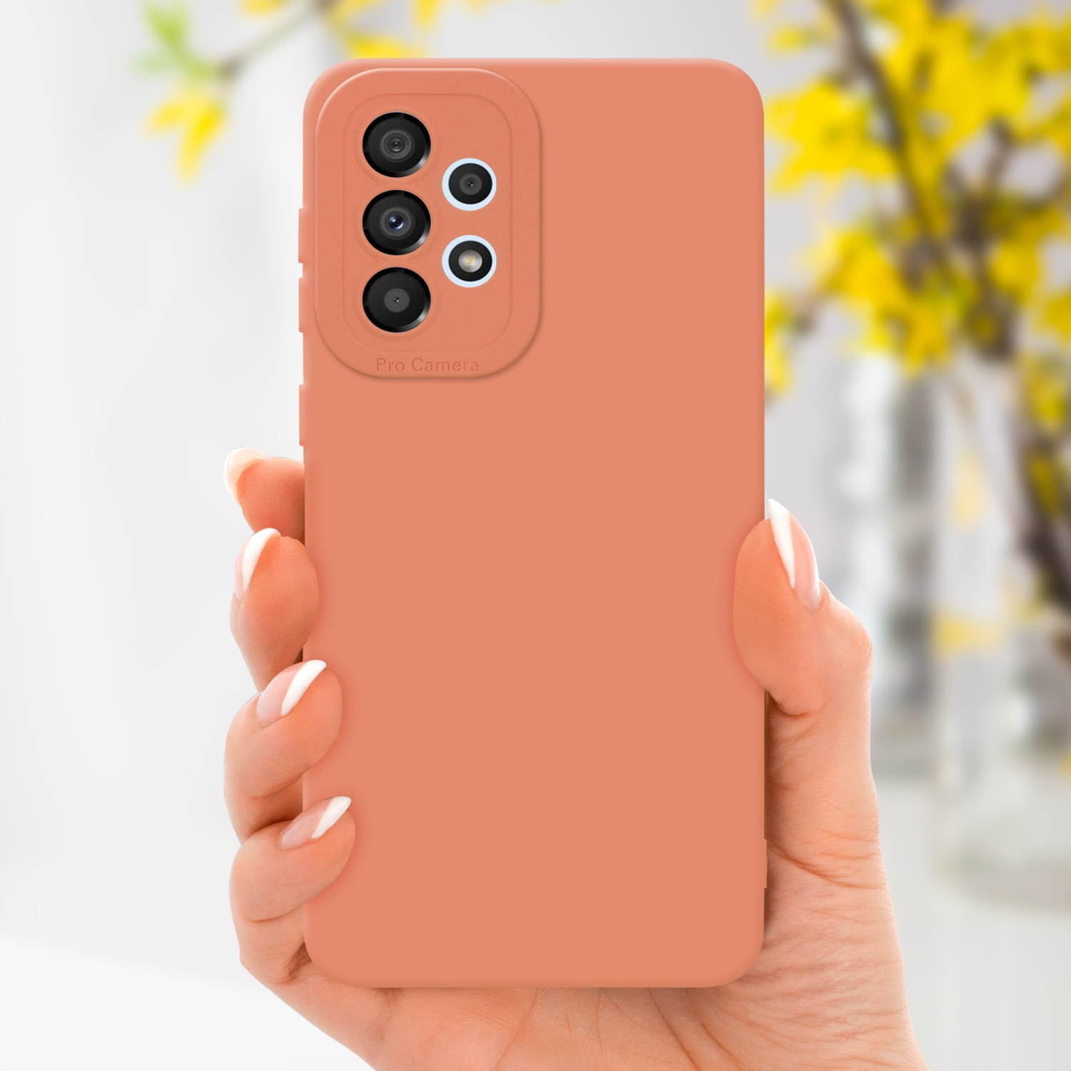 Una custodia per telefono color pesca è tenuta in mano. Fiori gialli sullo sfondo.