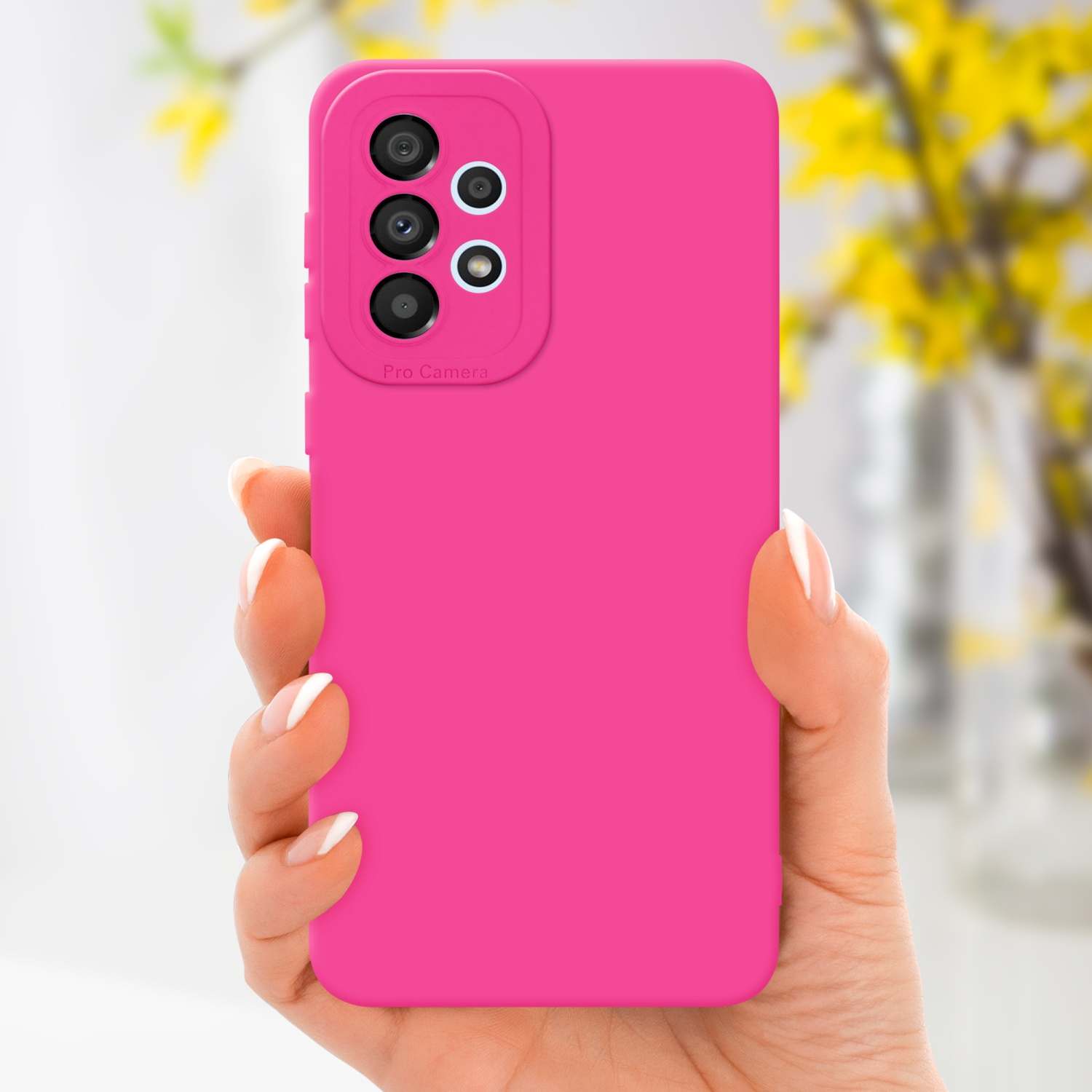 Una mano che tiene uno smartphone rosa con una fotocamera a tre lenti. Fiori gialli sullo sfondo sfocato.