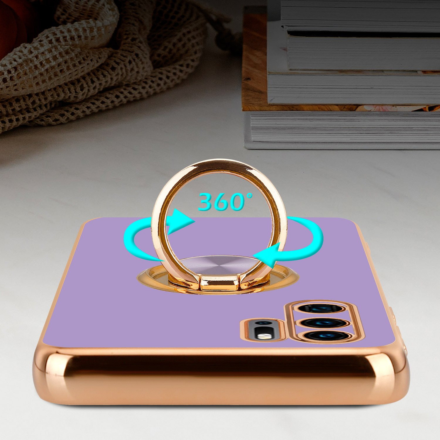 Lila Handyhülle mit goldenem Ringhalter, 360° Drehung, auf weißem Tisch, Bücher im Hintergrund.