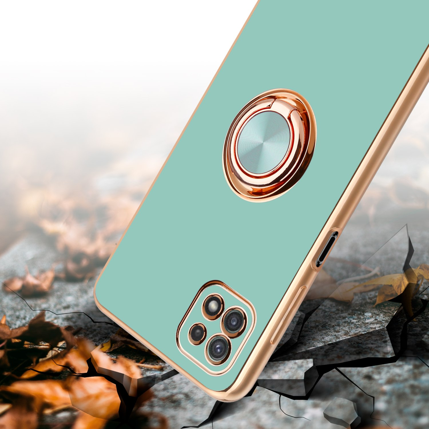 Eine mintgrüne Handyhülle mit goldenem Ringhalter auf einer zerbrochenen Oberfläche. Der Hintergrund ist unscharf.