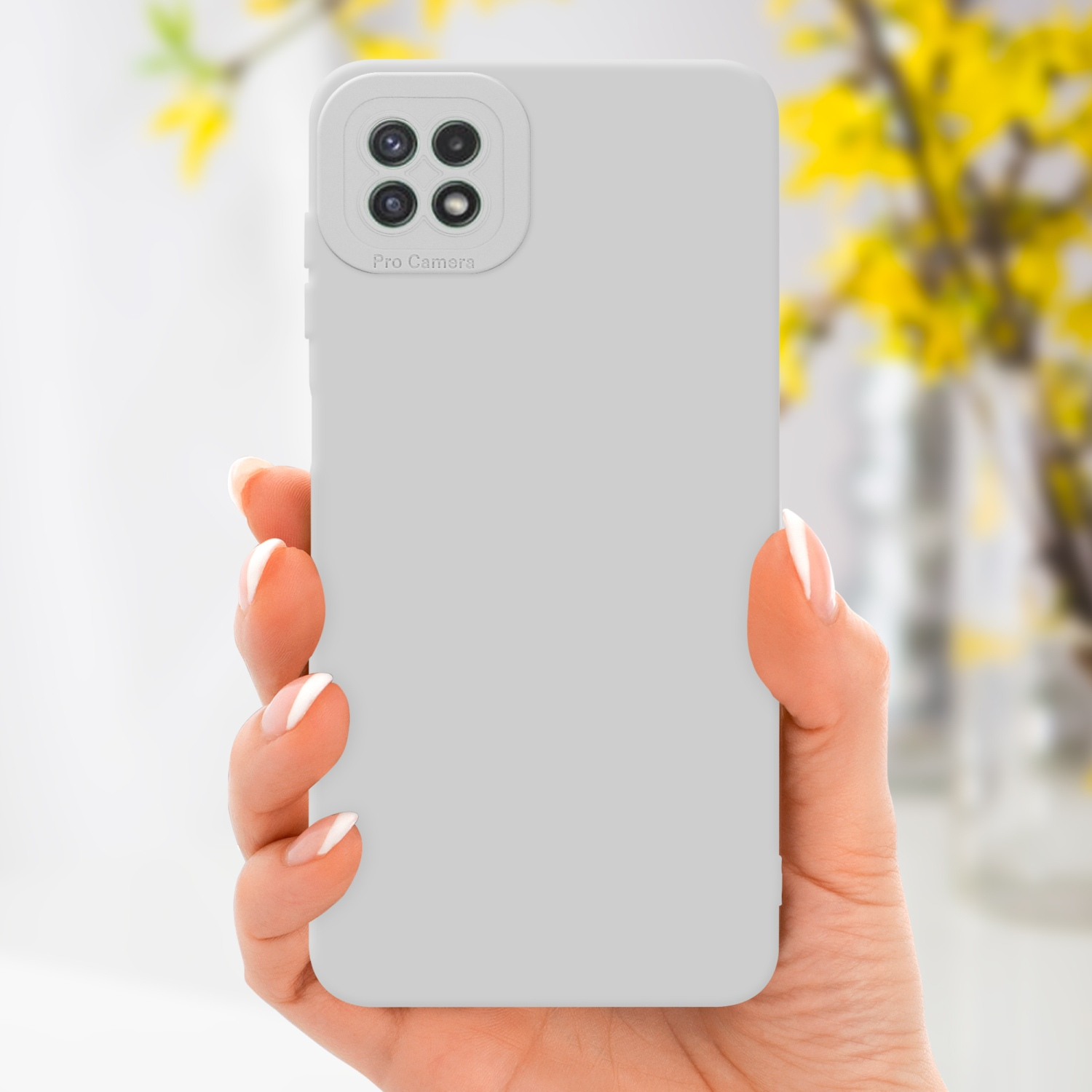 Mano che tiene una custodia per telefono grigio chiaro con lenti della fotocamera; fiori gialli sfocati sullo sfondo.