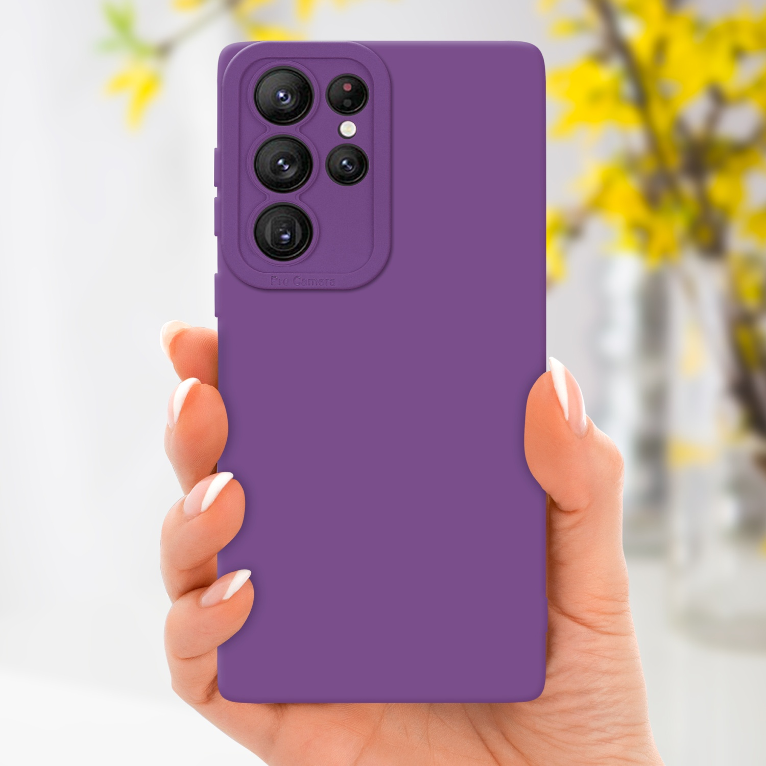 Mano che tiene una custodia viola con etichetta Pro Camera. Fiori gialli sfocati sullo sfondo.