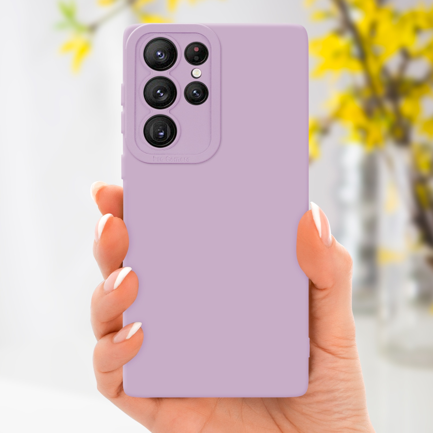 Une main tient une coque de téléphone violet clair avec une bosse pour la caméra. Fleurs jaunes floues en arrière-plan.