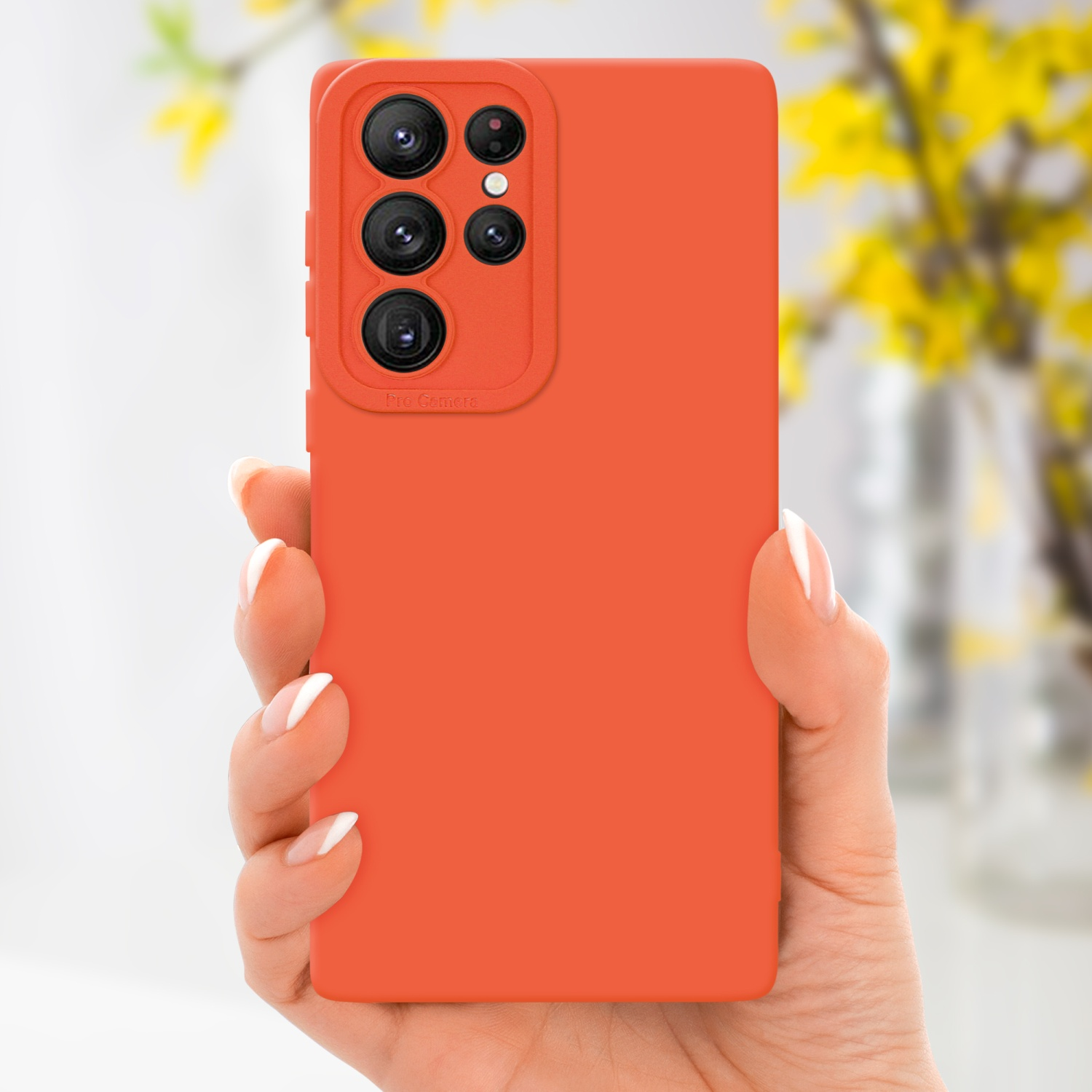 Main tenant une coque orange. Des fleurs jaunes sont en arrière-plan.