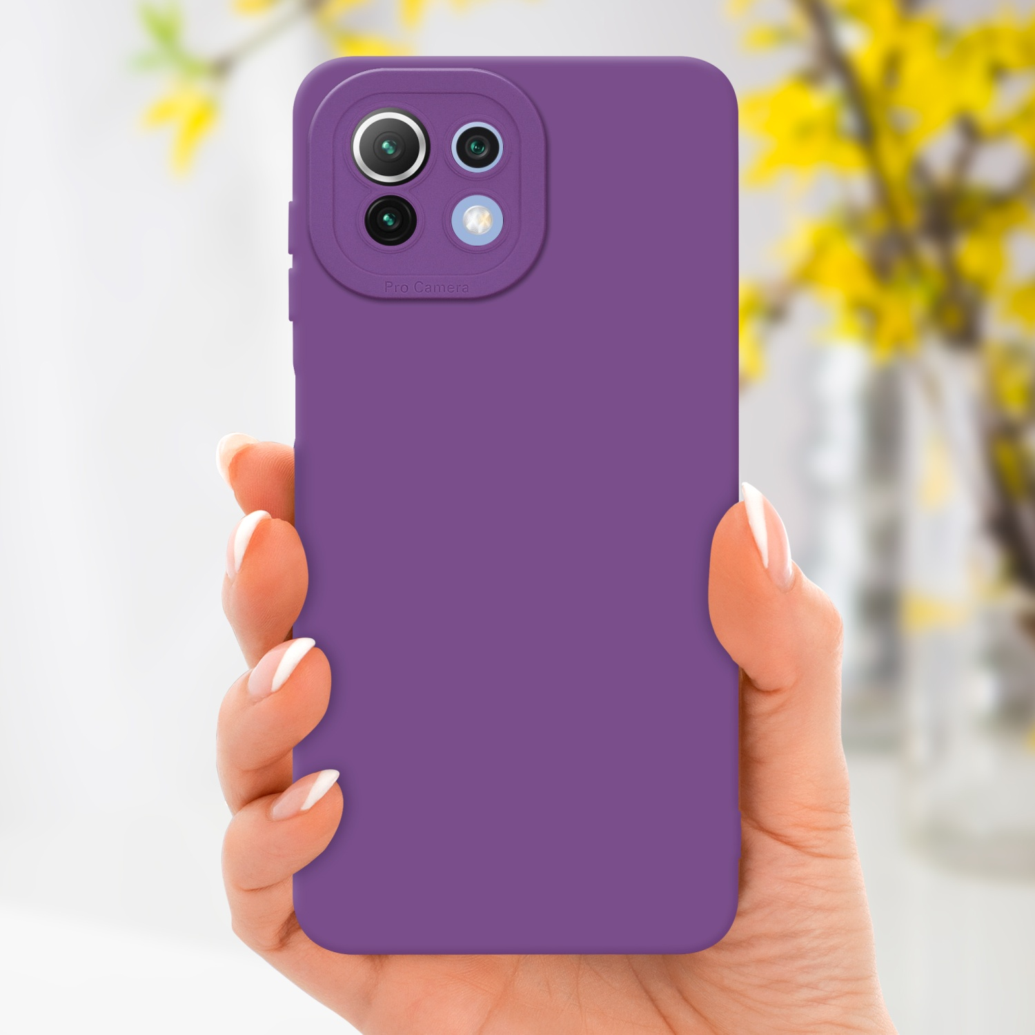 Une main tenant une coque de téléphone violette avec un module caméra. Fleurs jaunes en arrière-plan.