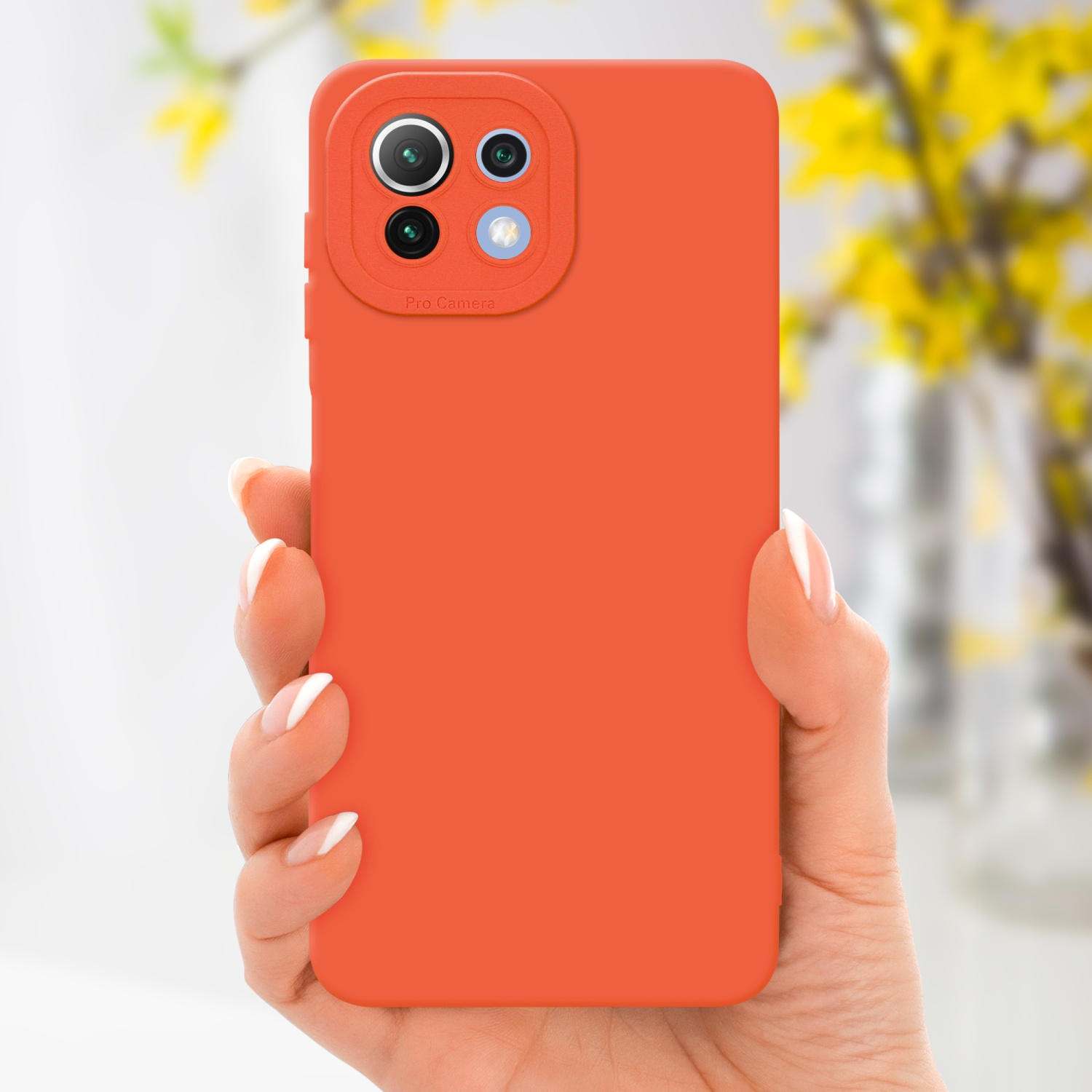 Mano che tiene una custodia arancione con fotocamera pro, fiori gialli sullo sfondo.