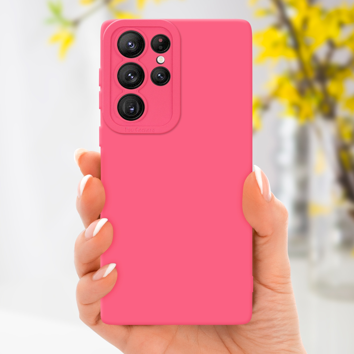 Mano che tiene una custodia rosa con modulo fotocamera, fiori gialli sullo sfondo.