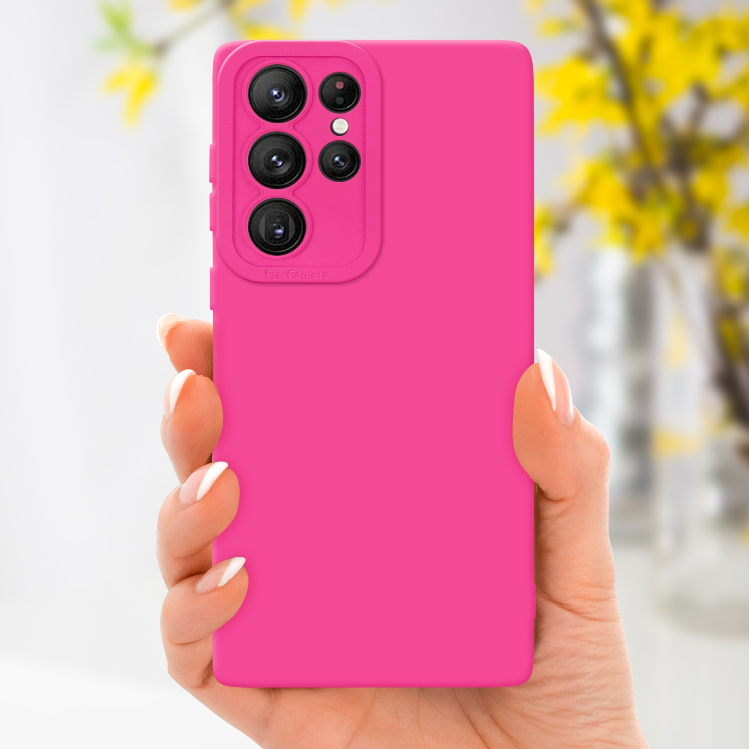 Una mano tiene una custodia rosa per telefono. La custodia ha un ritaglio per la fotocamera. Lo sfondo sono fiori sfocati.