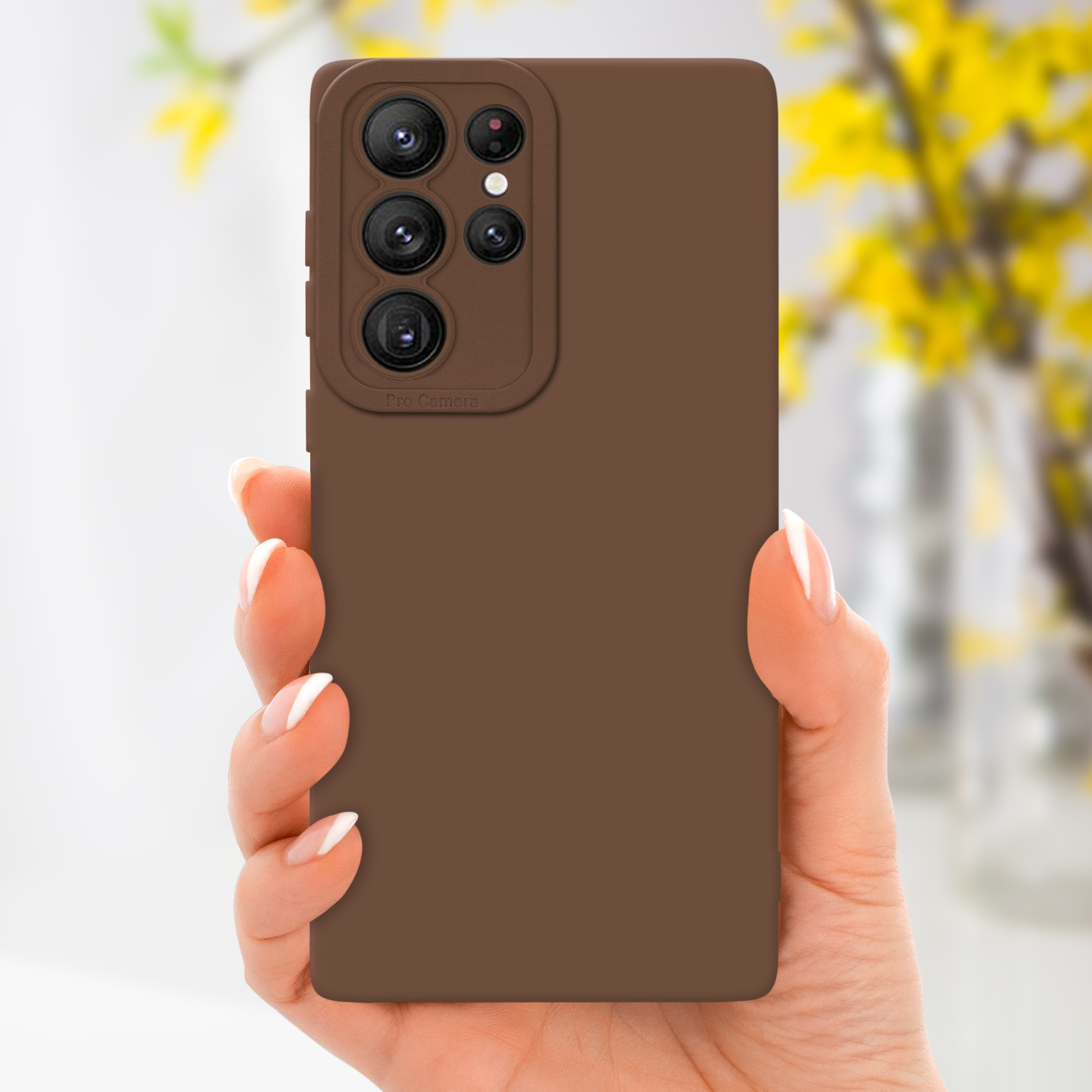 Main tenant une coque marron avec caméra, avec des fleurs en arrière-plan.