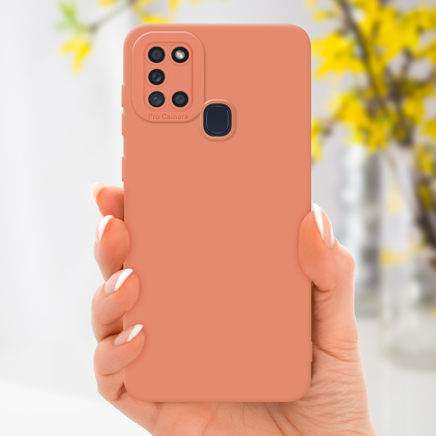 Una mano tiene una custodia per telefono color pesca. Uno sfondo sfocato mostra fiori gialli.