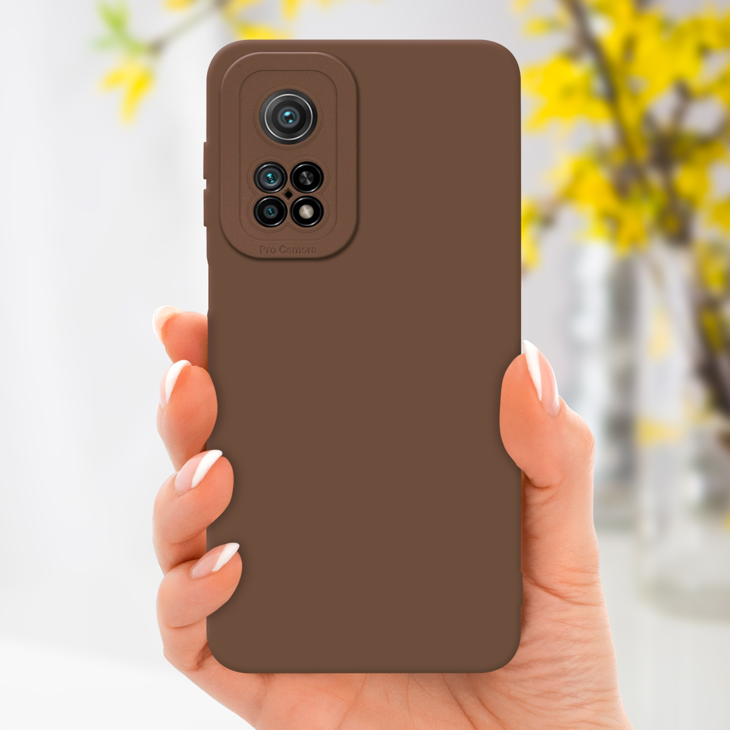 Una mano tiene una custodia marrone con modulo fotocamera. Fiori gialli sullo sfondo sfocato.