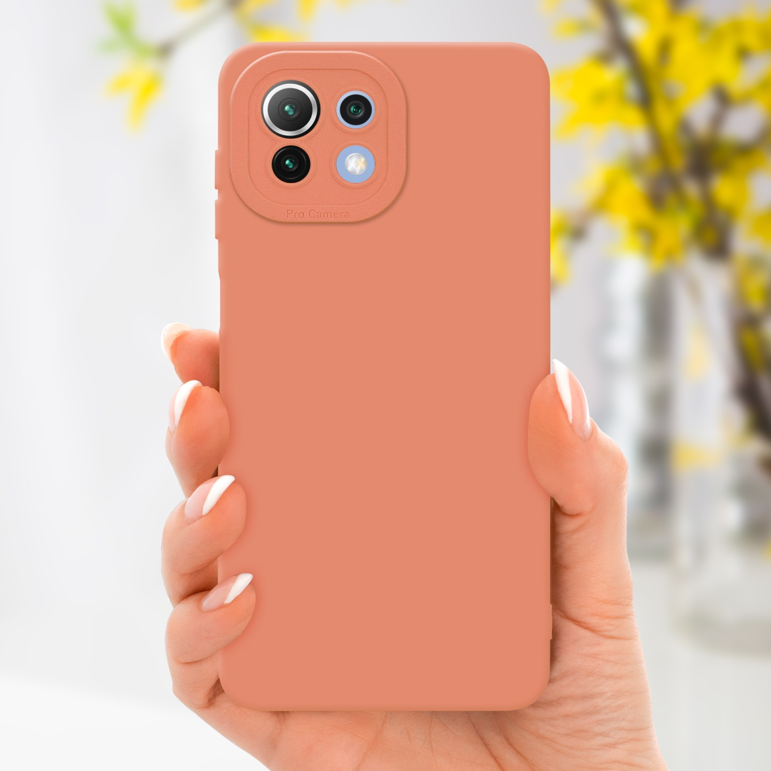 Una mano che tiene una custodia per telefono color corallo. Un'arrangiamento floreale giallo è sfocato sullo sfondo.