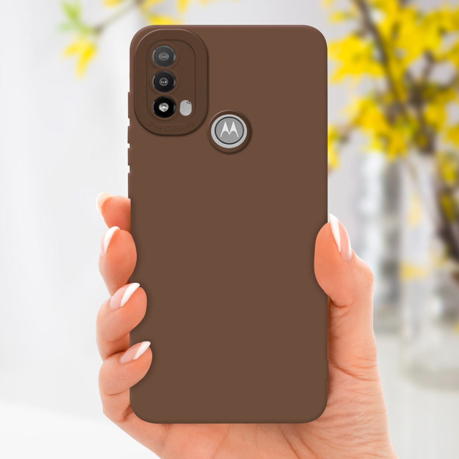 Una mano che tiene una custodia per telefono marrone con un proteggi fotocamera. Fiori gialli sfocati.