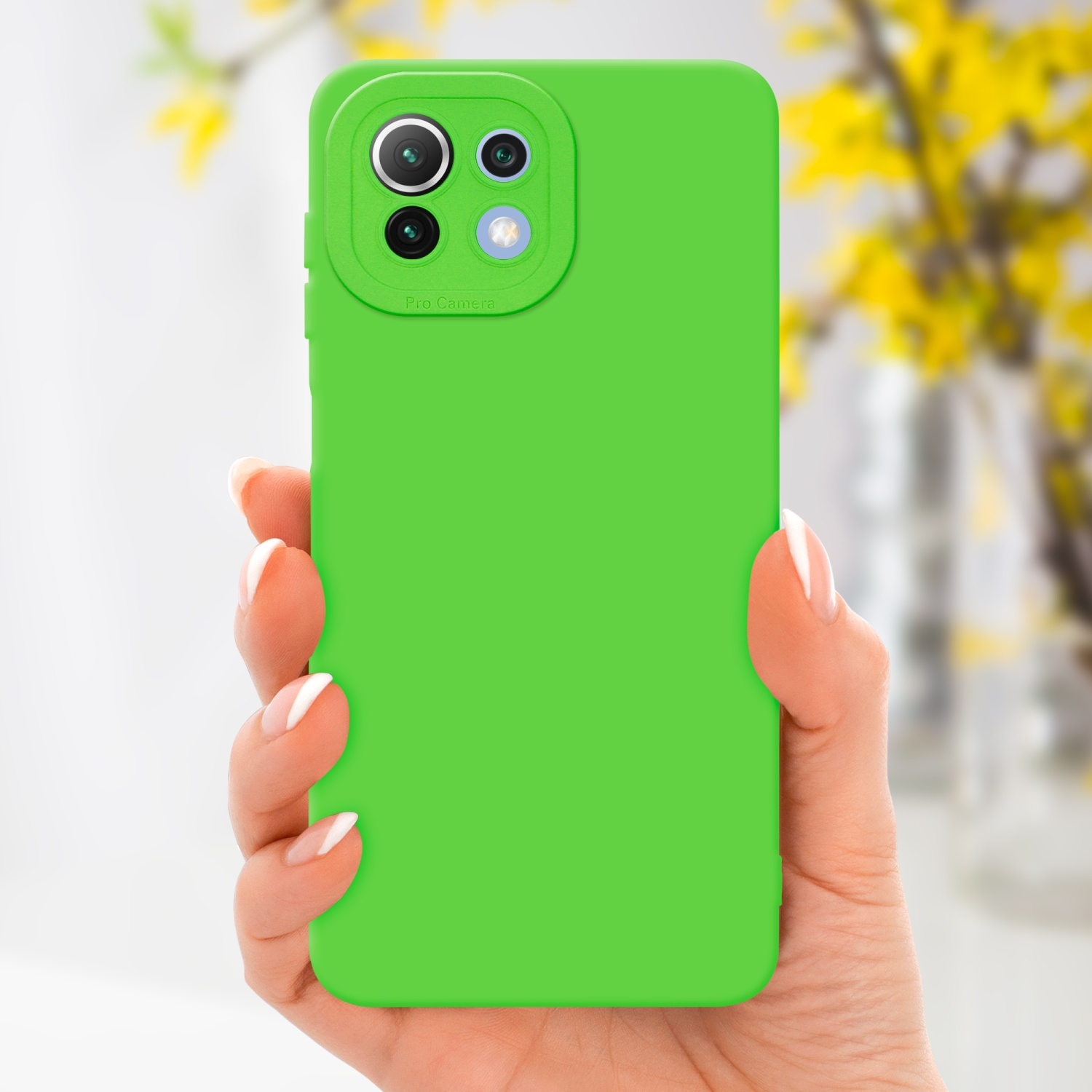 Una mano tiene una custodia verde brillante. Fiori gialli sullo sfondo sfocato.