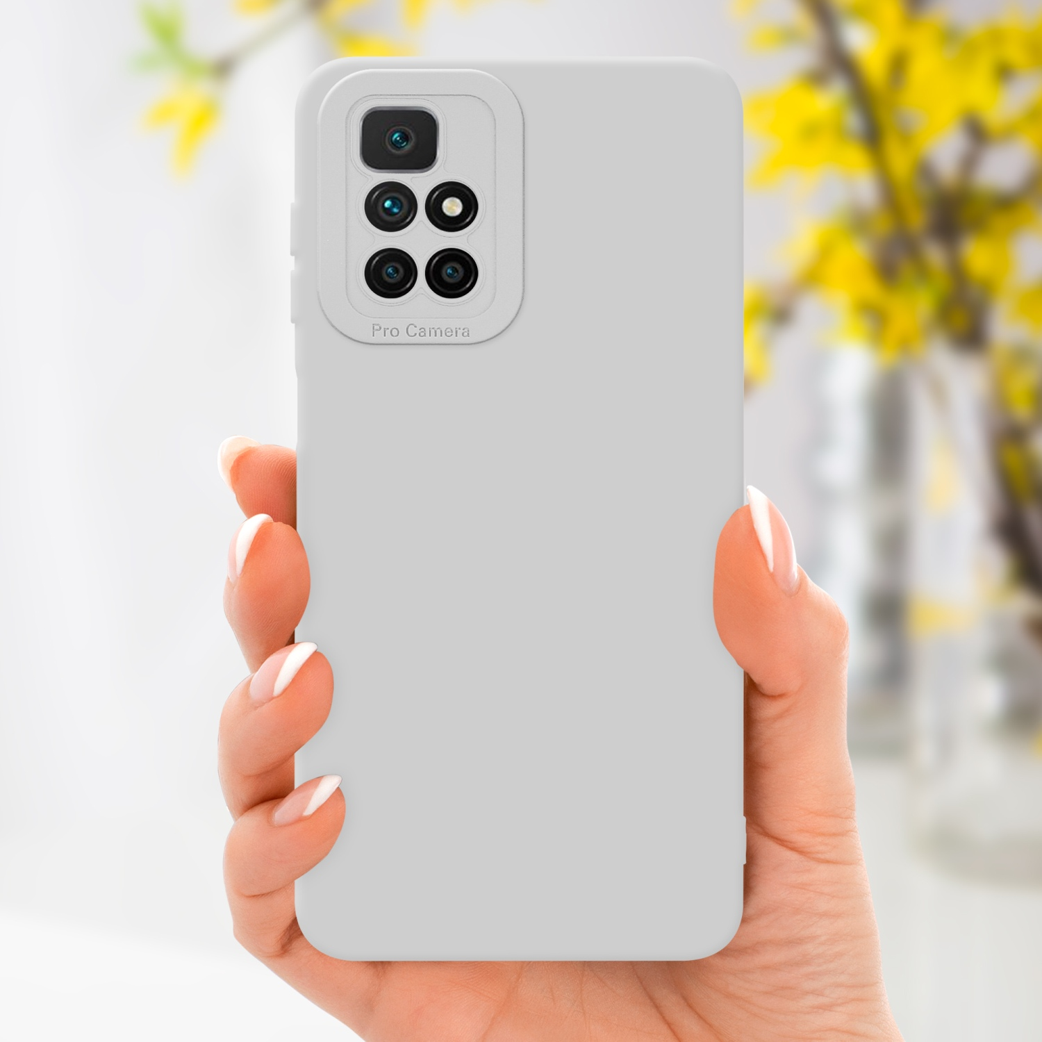 Main tenant une coque grise avec caméra, avec des fleurs en arrière-plan.