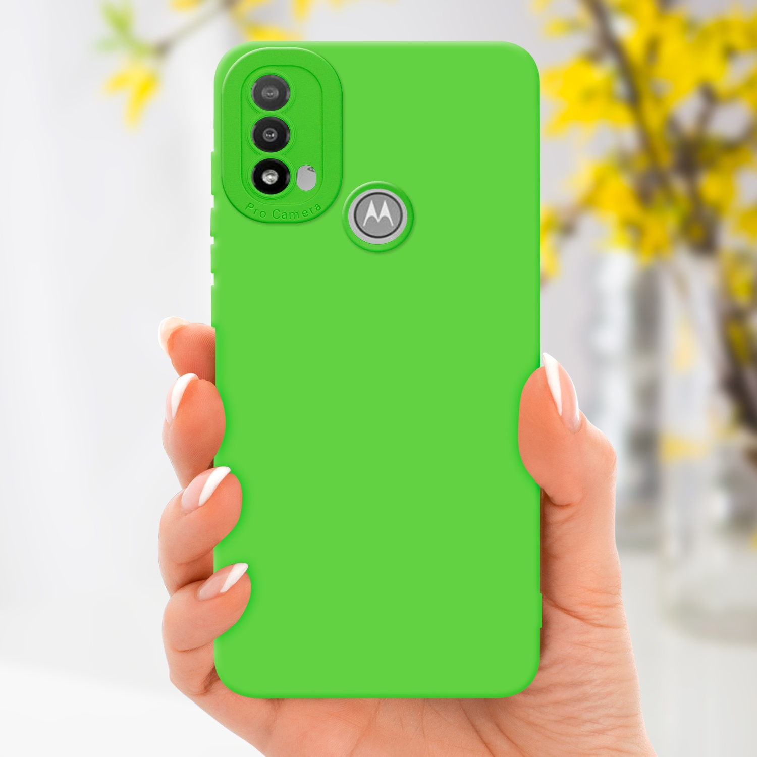 Una custodia per telefono verde tenuta in mano. La custodia ha un rilievo per la fotocamera. Fiori gialli sfocati sullo sfondo.