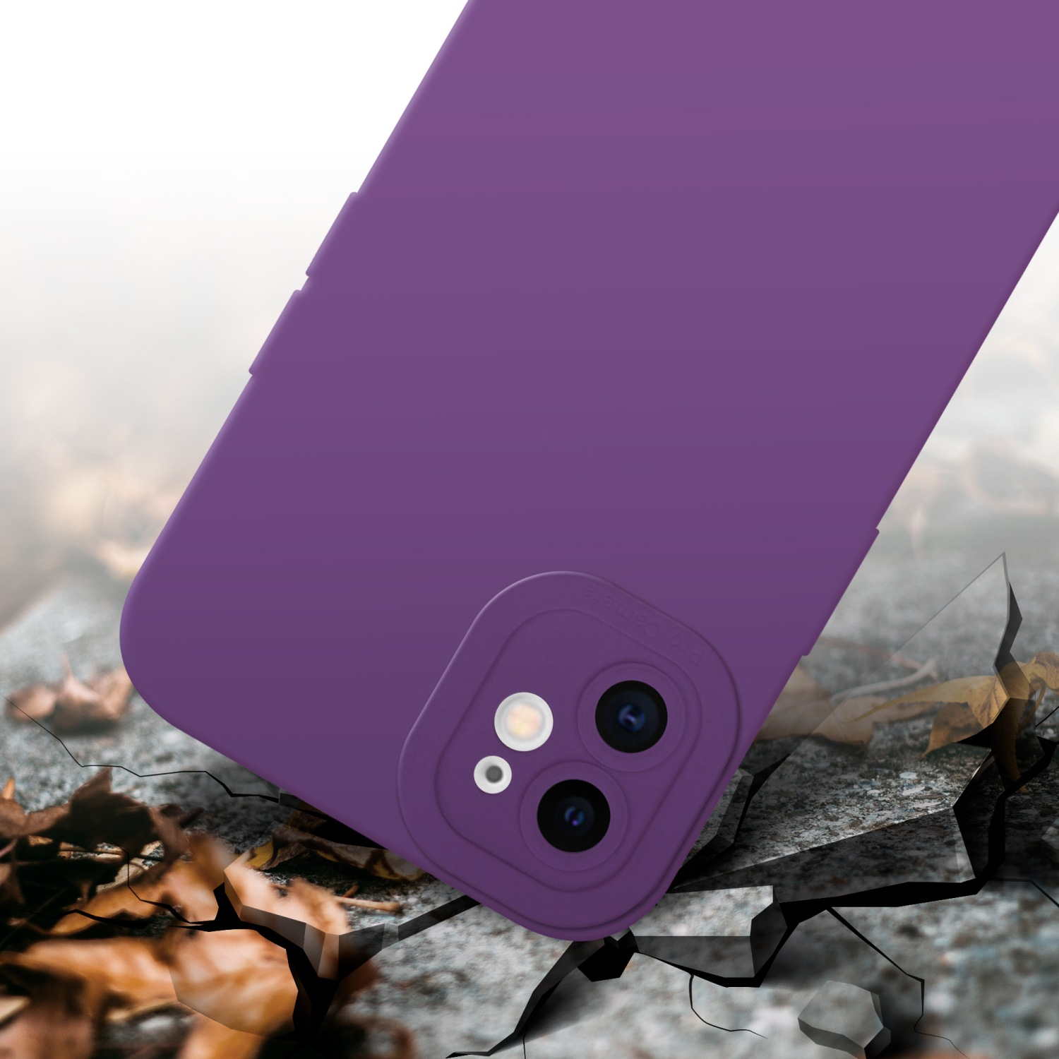 Custodia viola su terreno crepato. Dettaglio della fotocamera sulla custodia. Foglie marroni intorno.
