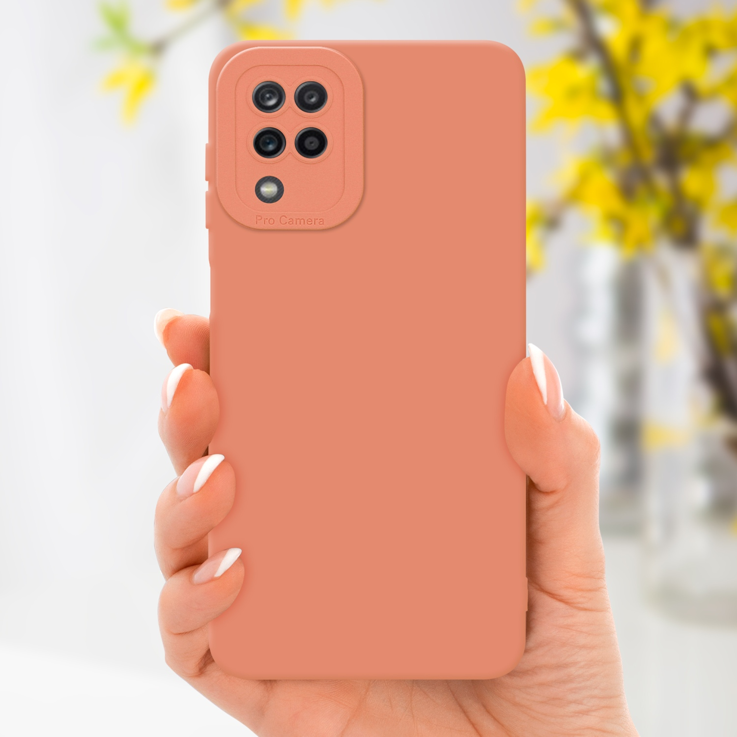 Una custodia color pesca per telefono tenuta in mano. Fiori gialli in un vaso sullo sfondo.