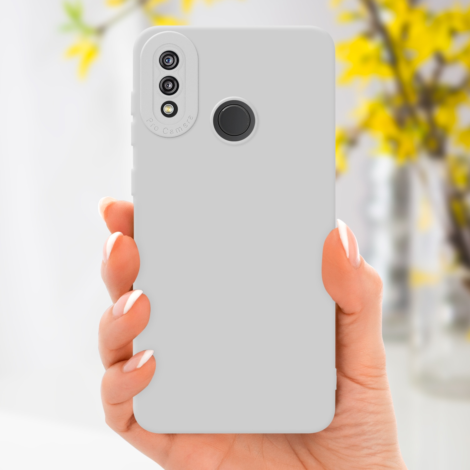 Una mano che tiene una custodia per telefono grigio chiaro con modulo fotocamera. Fiori gialli sullo sfondo.