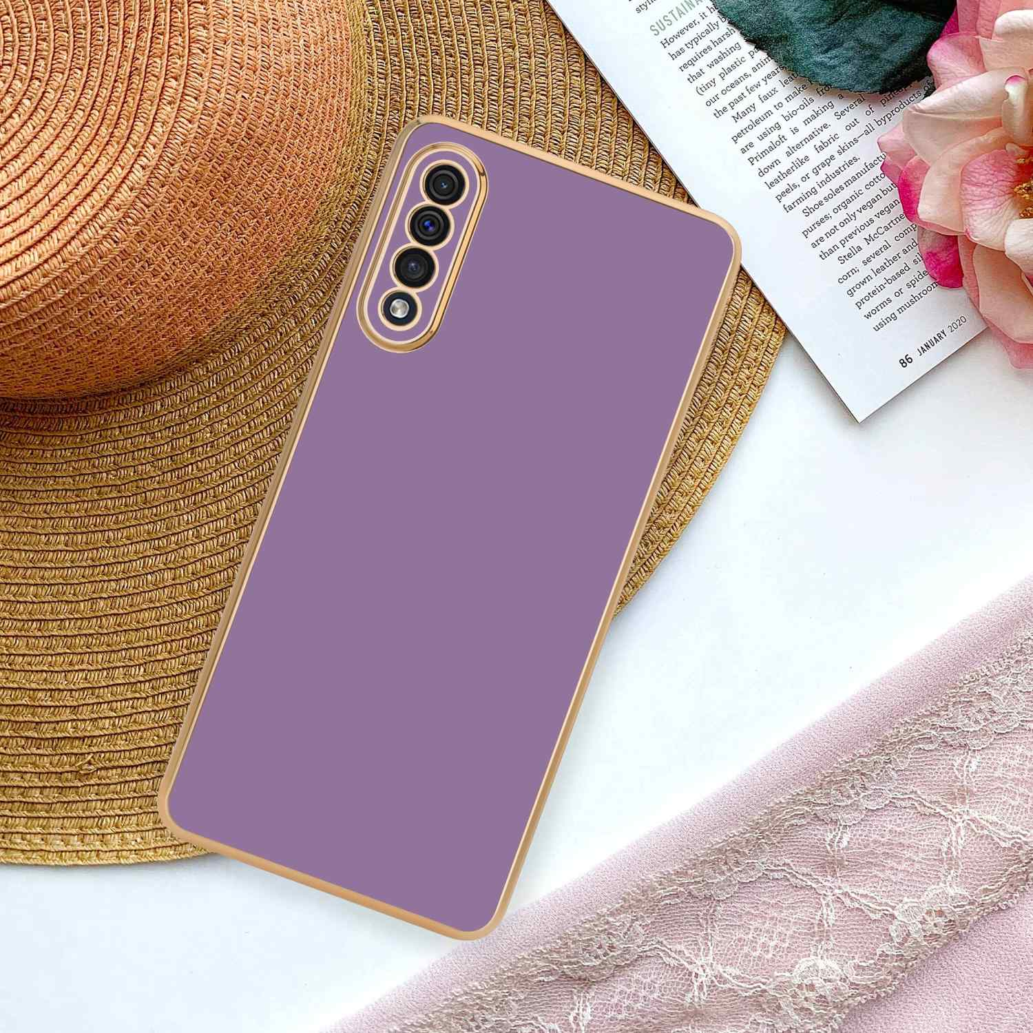 Telefon in lila Hülle, neben Hut, rosa Stoff und einer Zeitschrift.