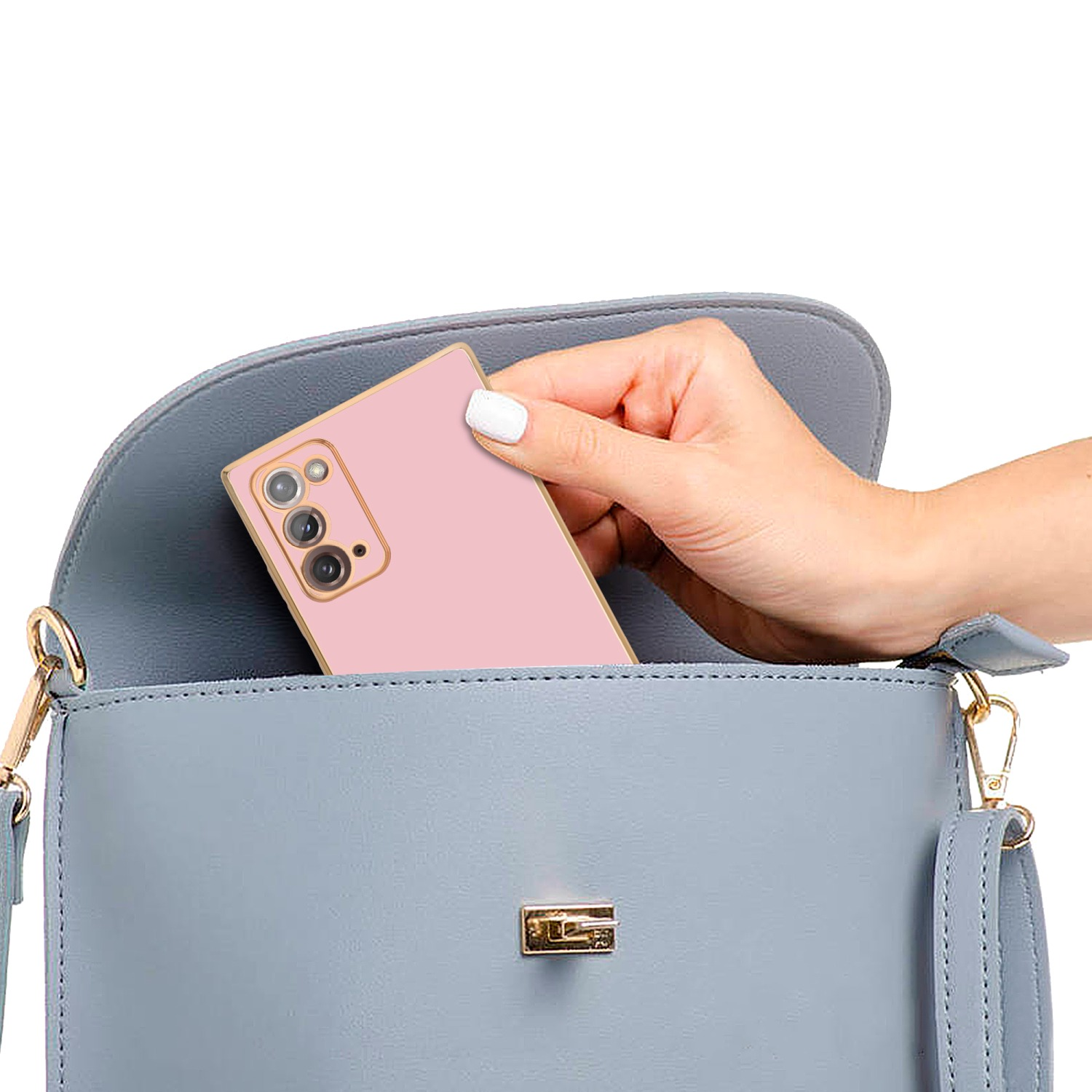 Hand steckt ein pinkfarbenes Telefon in eine hellblaue Handtasche. Die Tasche hat goldfarbene Beschläge.