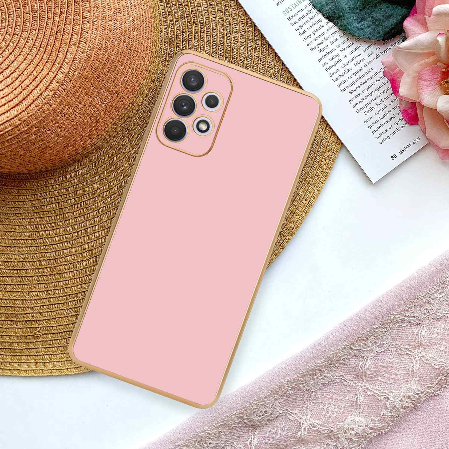 Rosa Telefon in einer goldfarbenen Hülle auf einem Strohhut und einer Zeitschrift.